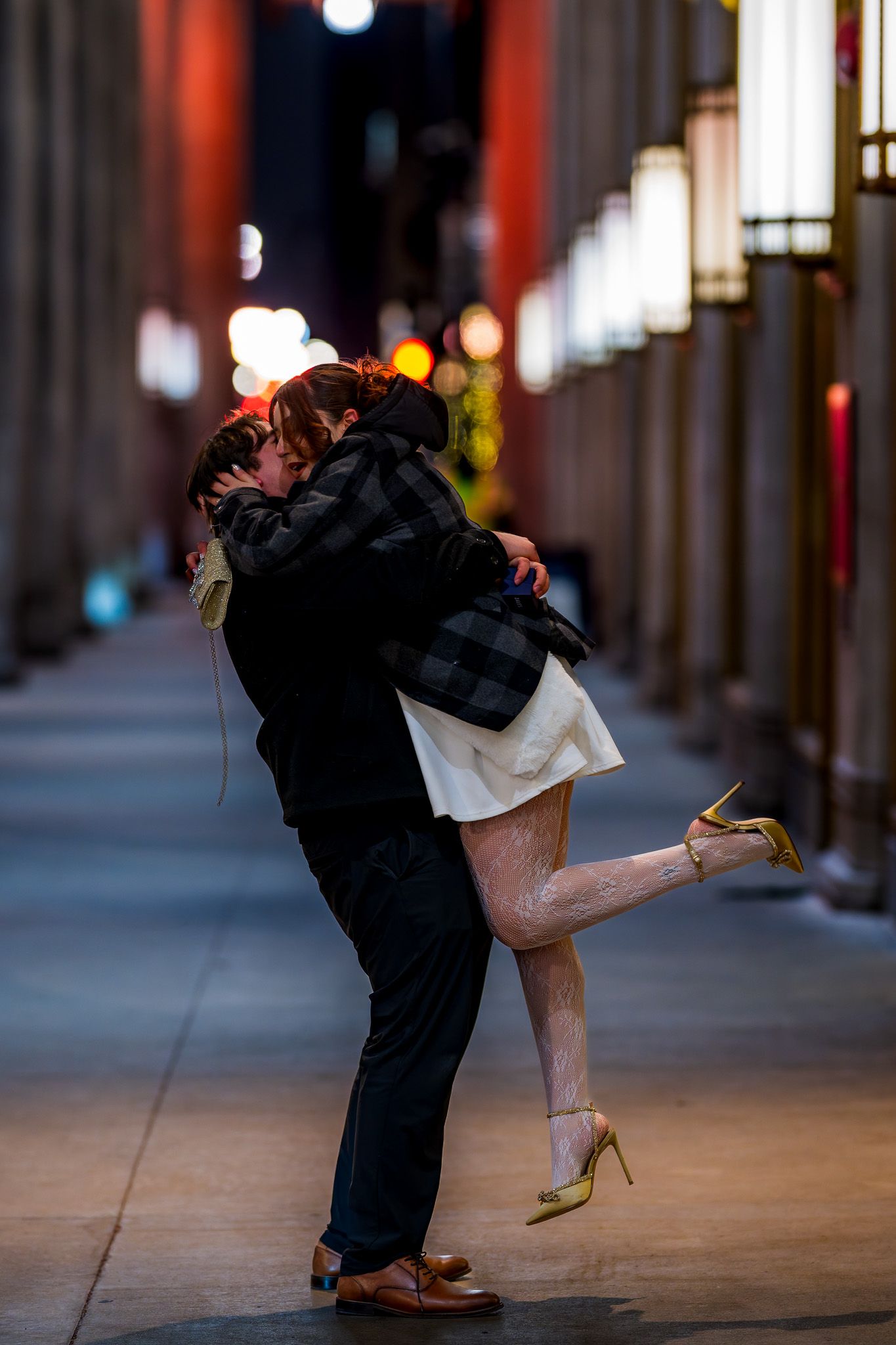Romantic couple sharing a lift and kiss in glowing city alley at night.