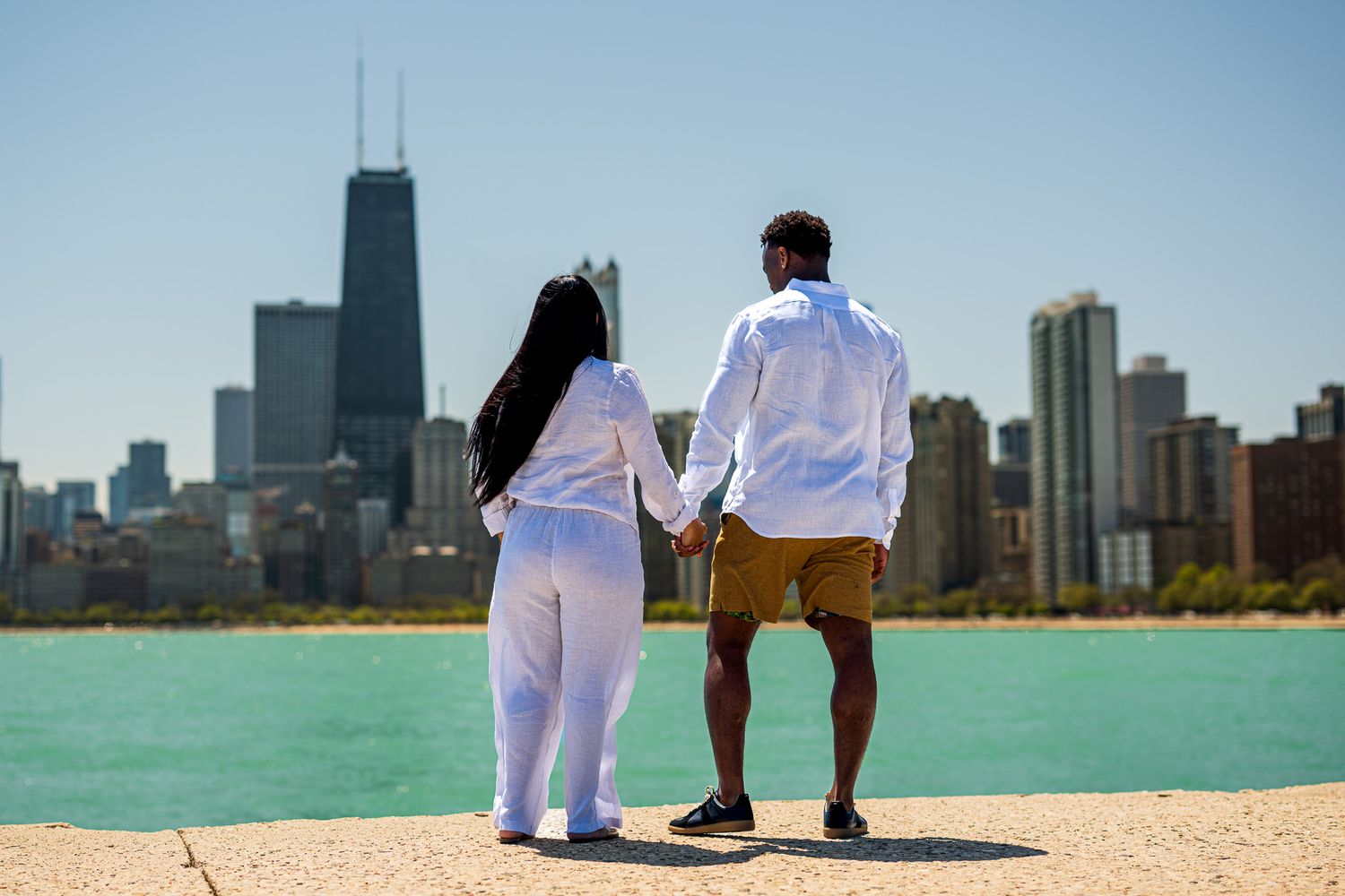 Couple holding hands facing Chicago skyline with John Hancock Tower on sunny day.