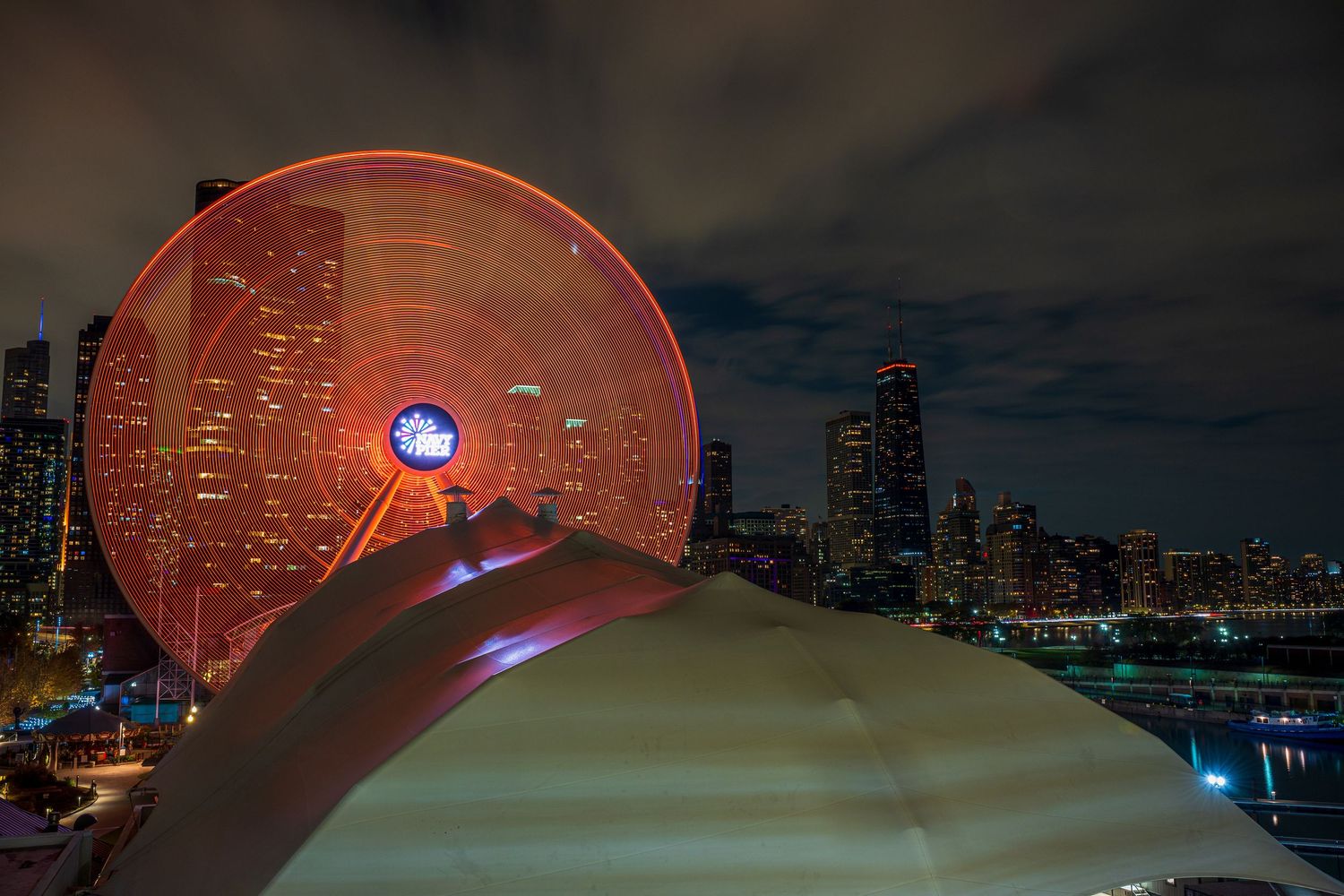 Illuminated Ferris wheel glowing red against Chicago skyline at night with city lights reflecting on the water.