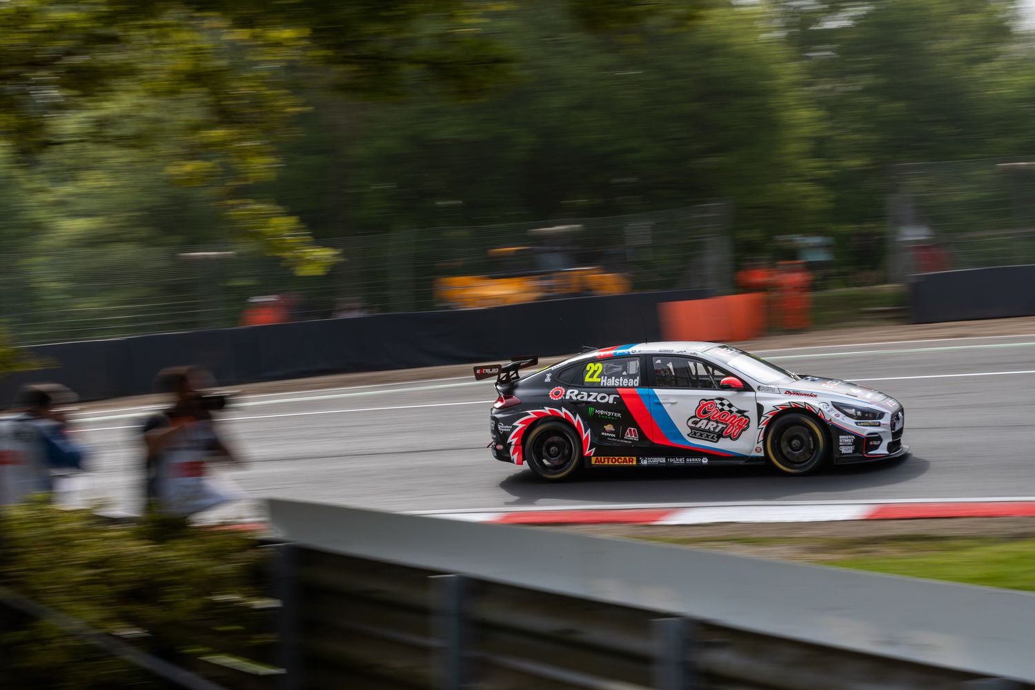 BMW BTCC race car competing on track with spectators visible in the background.