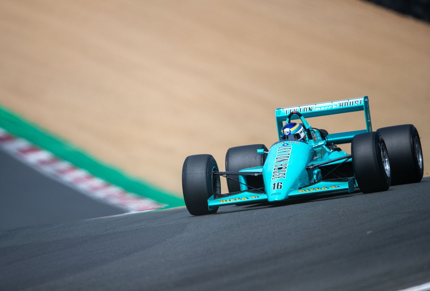A teal Formula 1 racing car numbered 16 speeding around a track corner during a professional motorsport event.