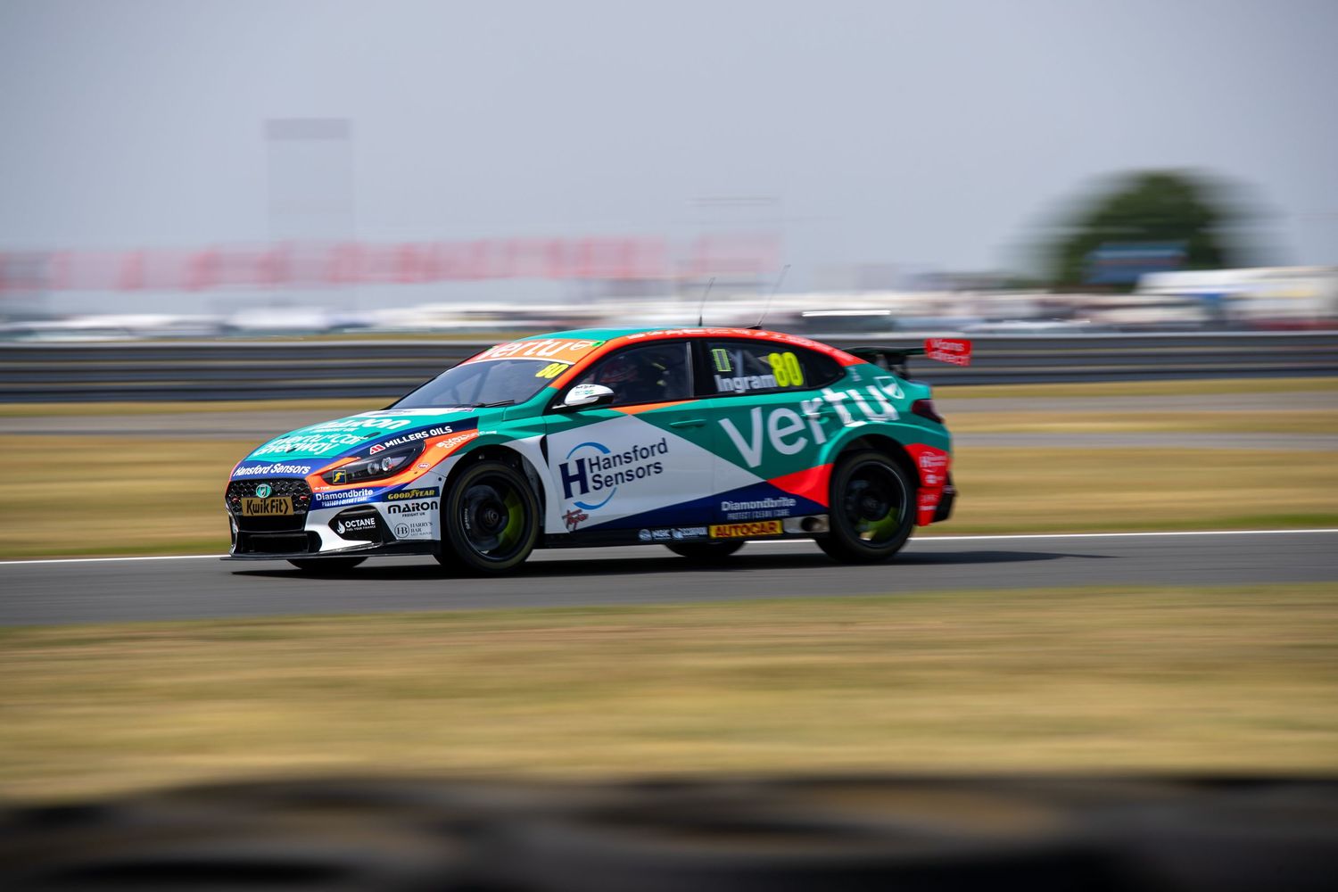 Vertu Motors BTCC racing car speeding on track during a British Touring Car Championship race at a sunny circuit.