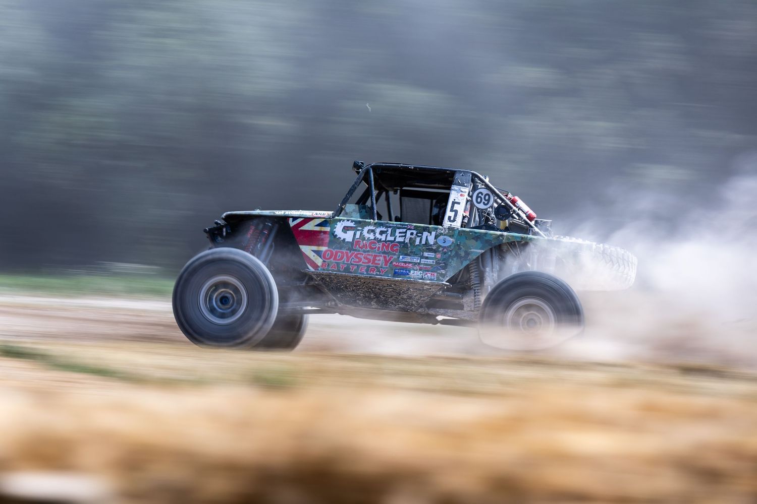 A racing off-road buggy speeds across a dirt track, kicking up dust and smoke during an intense rally race.