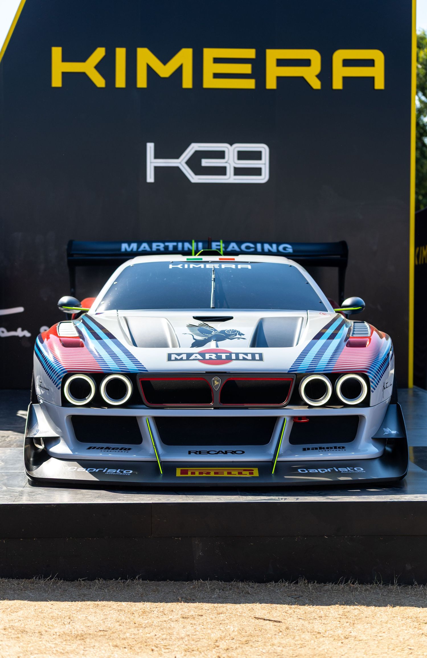 Kimera KE39 Martini Racing livery sports car displayed at an automotive event, featuring Pirelli tires and Recaro branding.