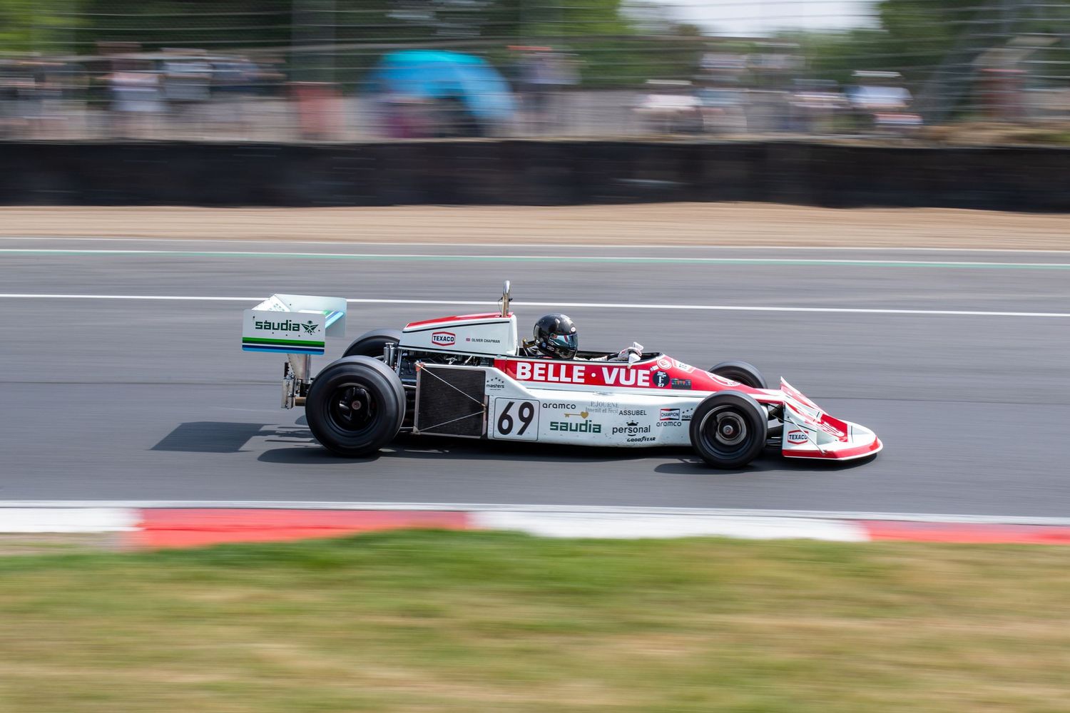 Vintage Formula racing car number 69 with Belle Vue livery speeding on a sunny race circuit.