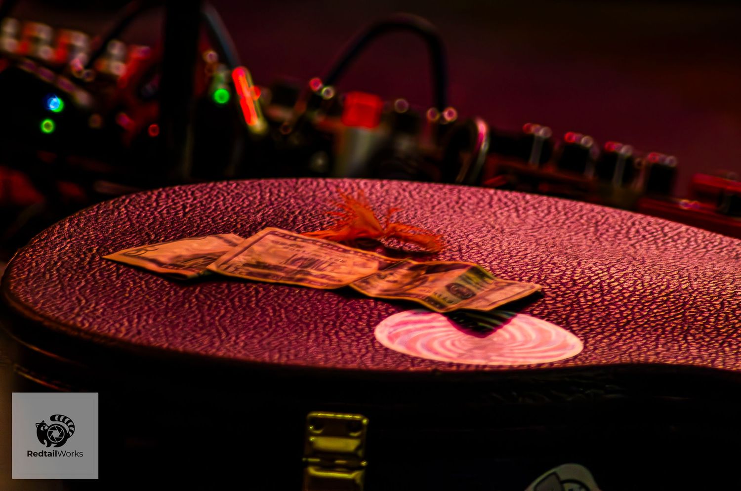 Guitar case with dollar bills resting inside under warm stage lighting.