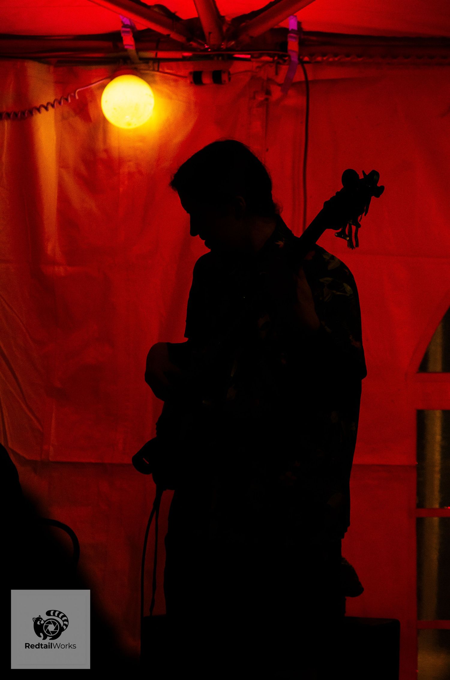 Silhouette of a guitarist performing on stage under a warm orange light with red backdrop.