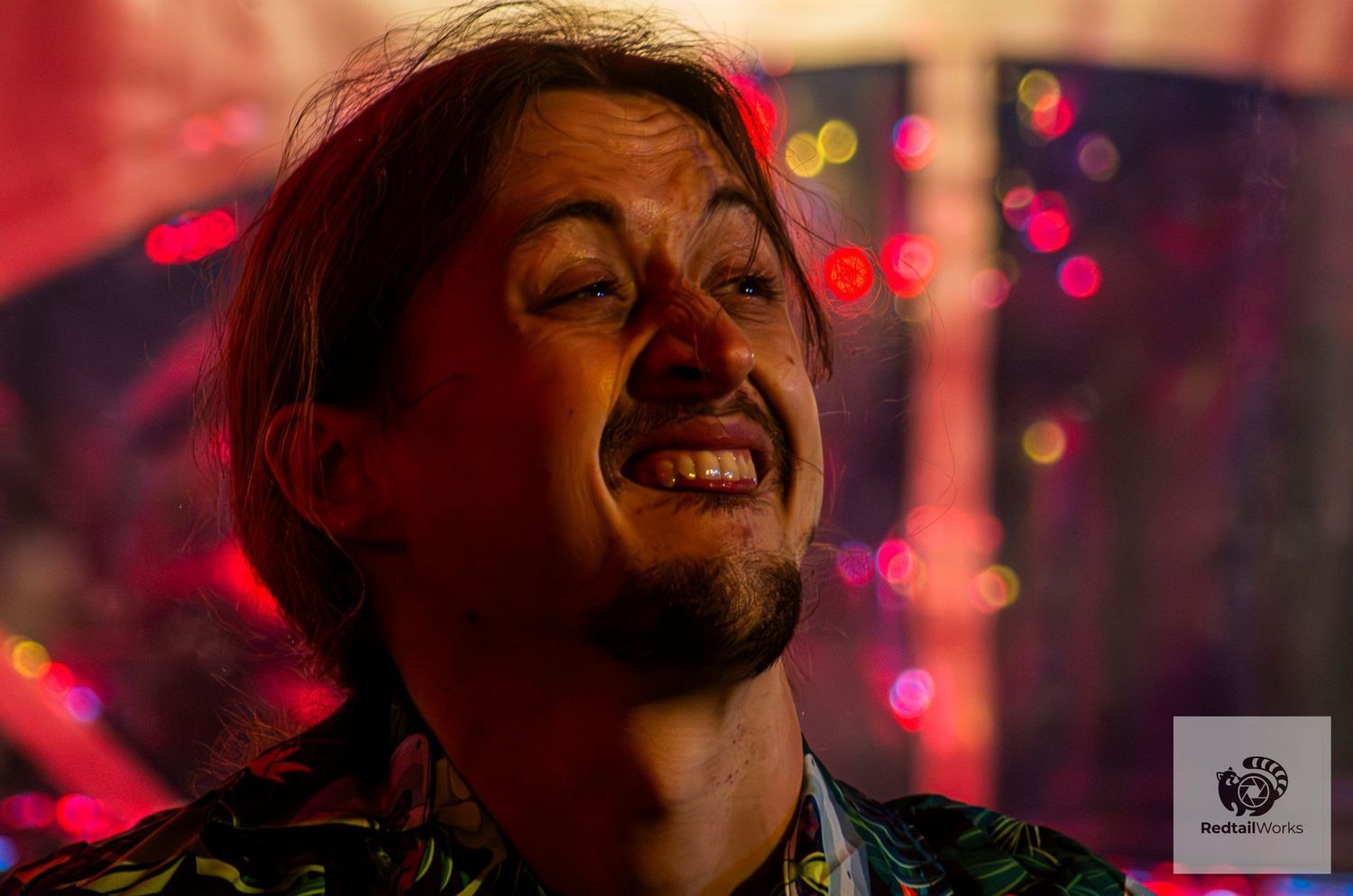 Male musician smiling joyfully on stage with colorful bokeh lights in the background.