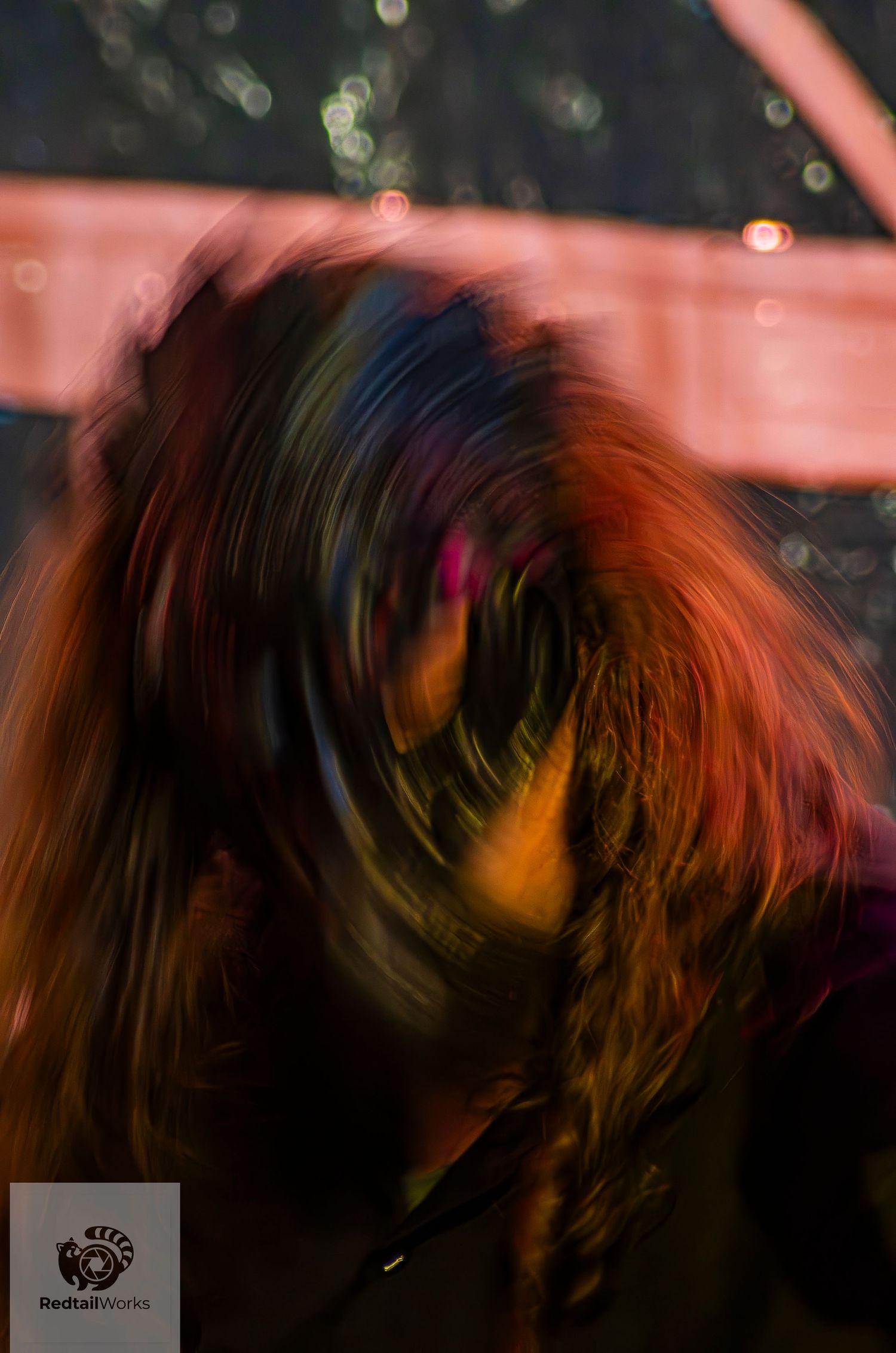 Motion blur portrait of a person with red hair spinning at a live music event.