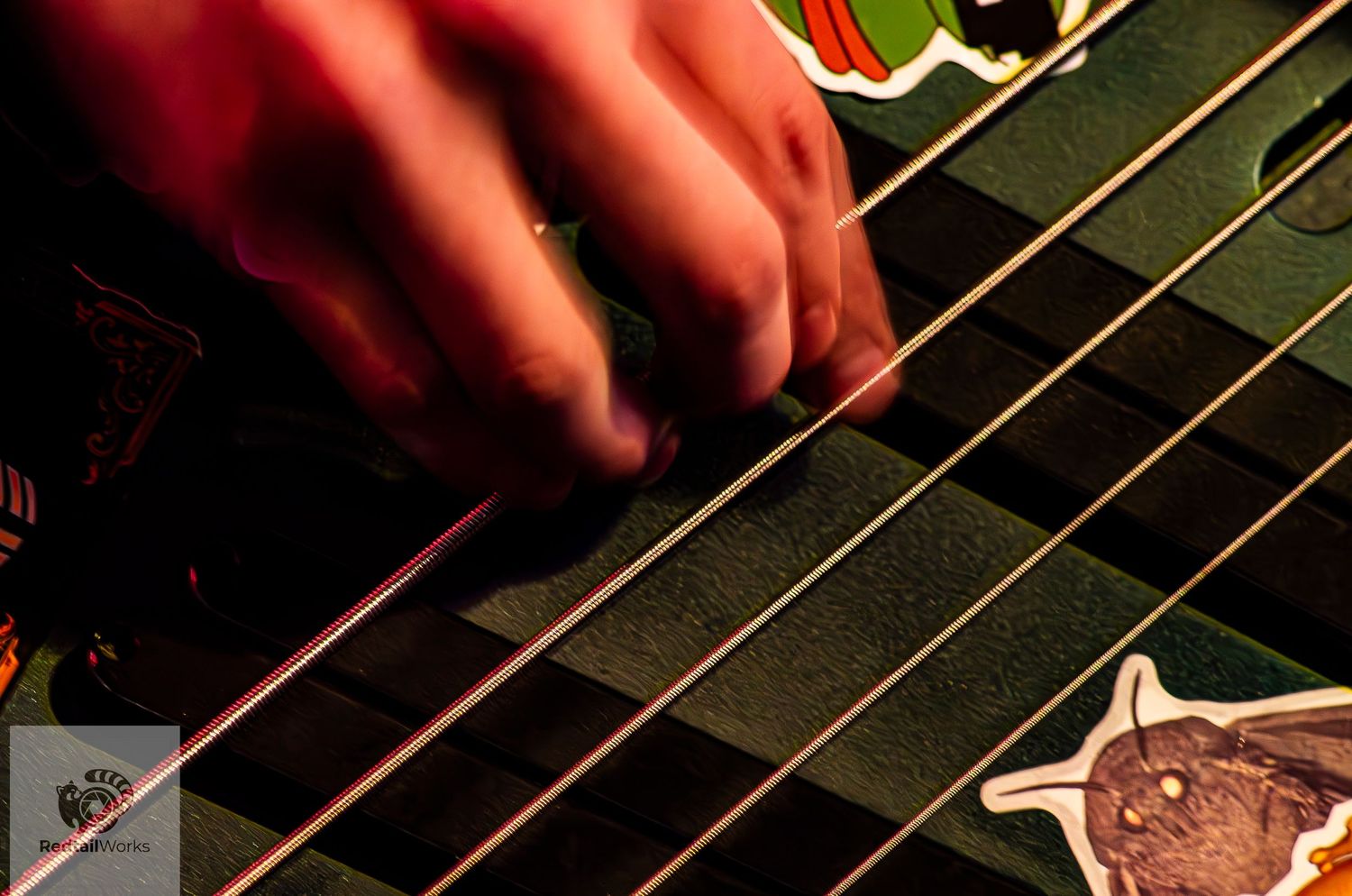 Musician's hand strumming strings of a sticker-covered guitar under dramatic stage lighting.