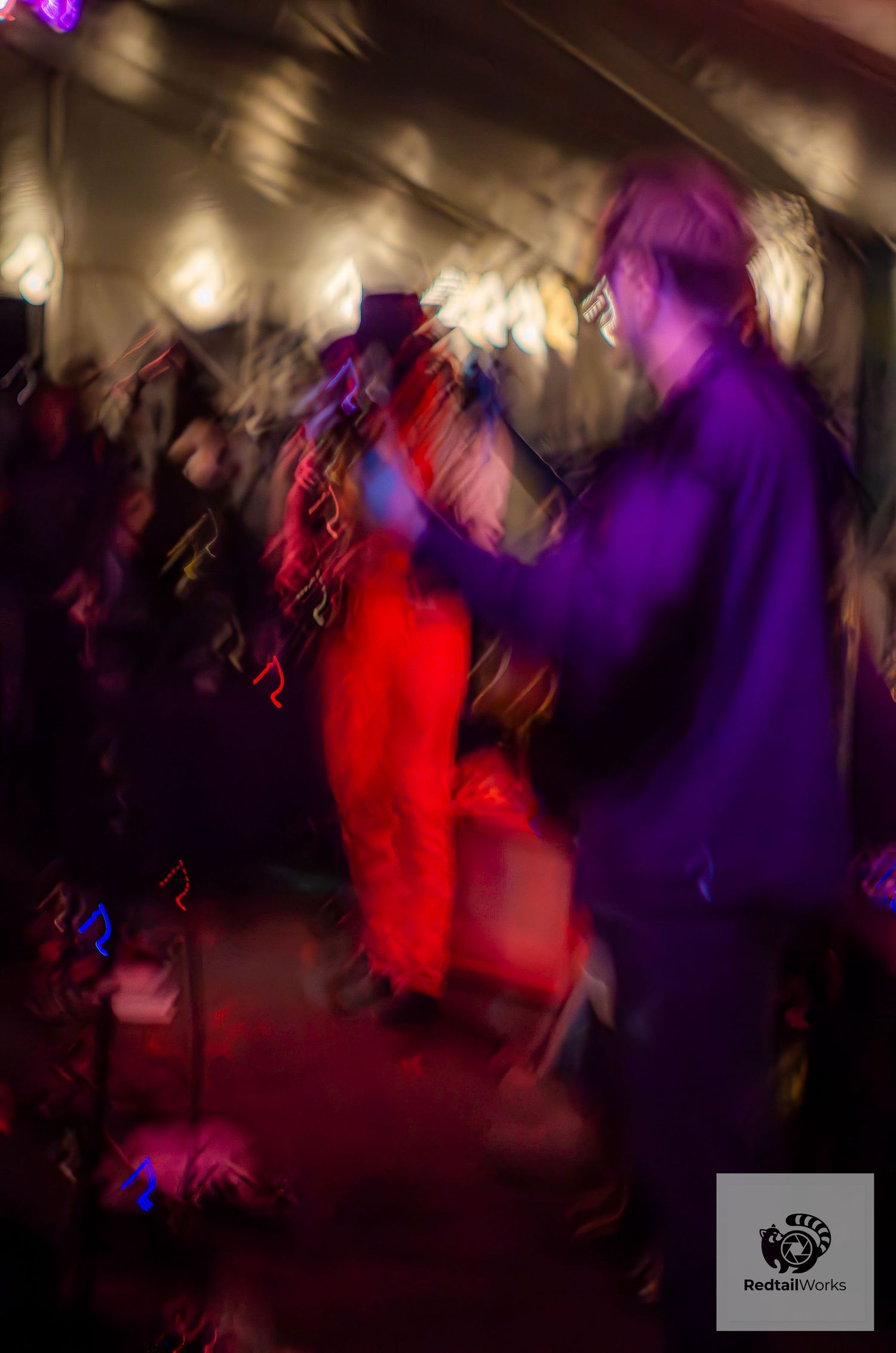 Blurred motion shot of performers on a vibrant stage with colorful lights and crowd.