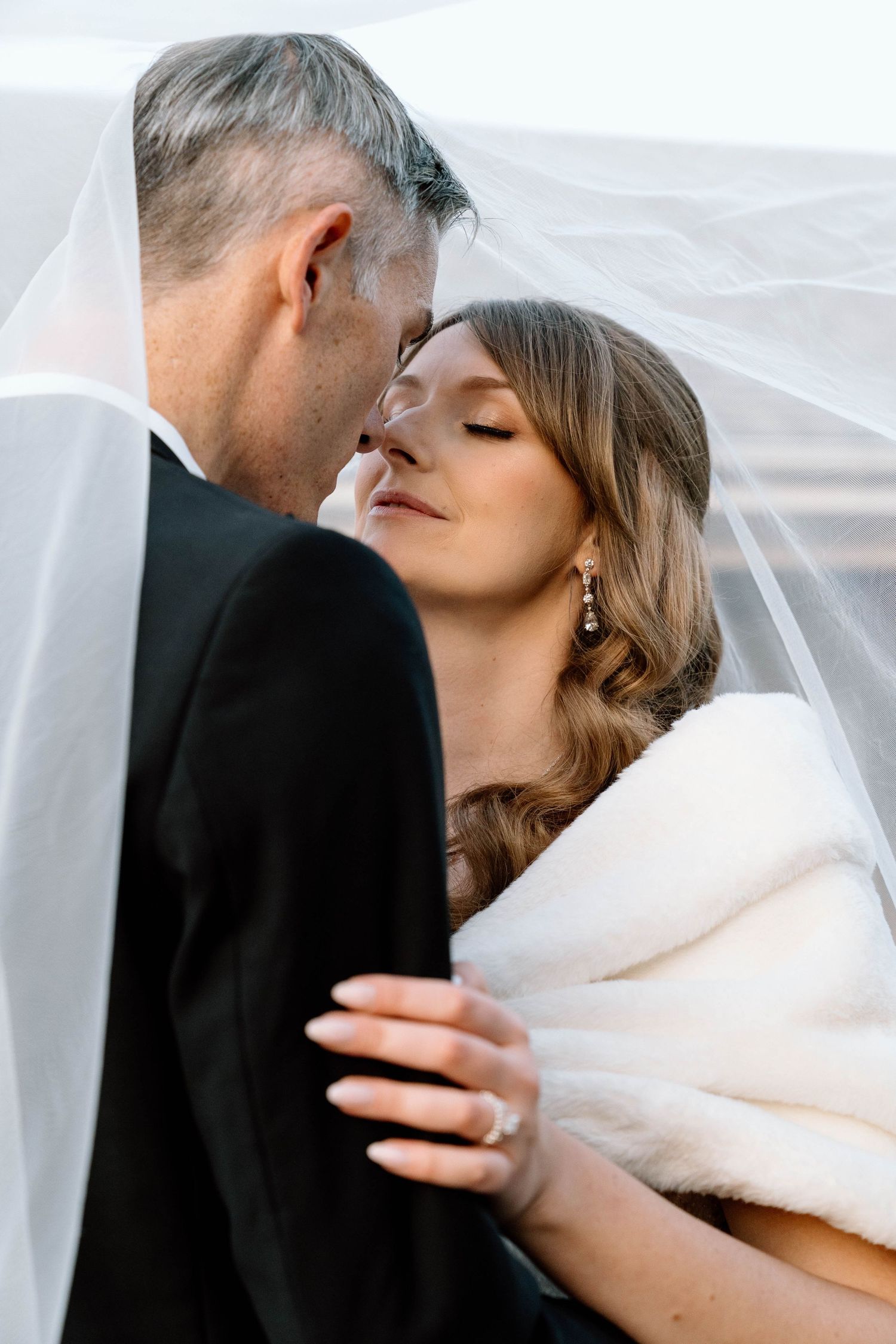 Bride and groom under a veil touching noses