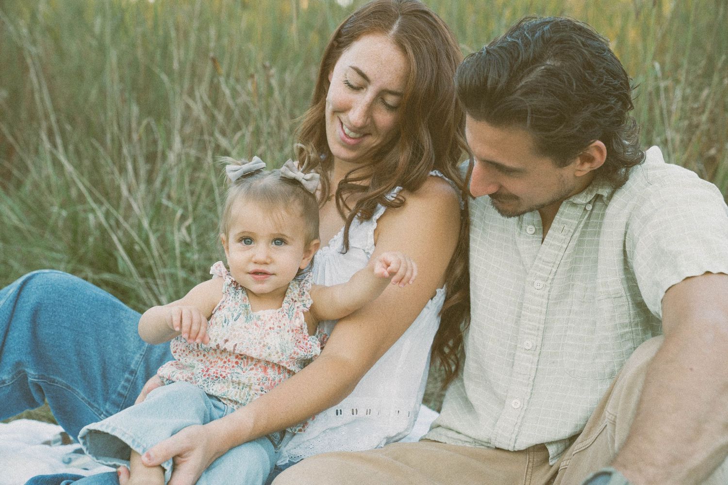 Mom, dad, and little girl sitting in a grass field