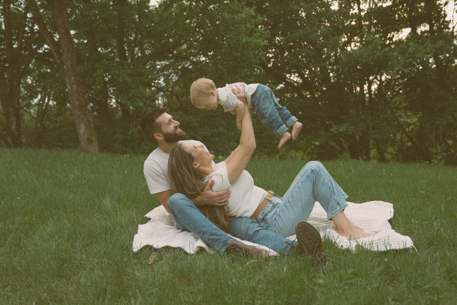 A woman lying on her husband's lap, smiling as she holds up her little boy