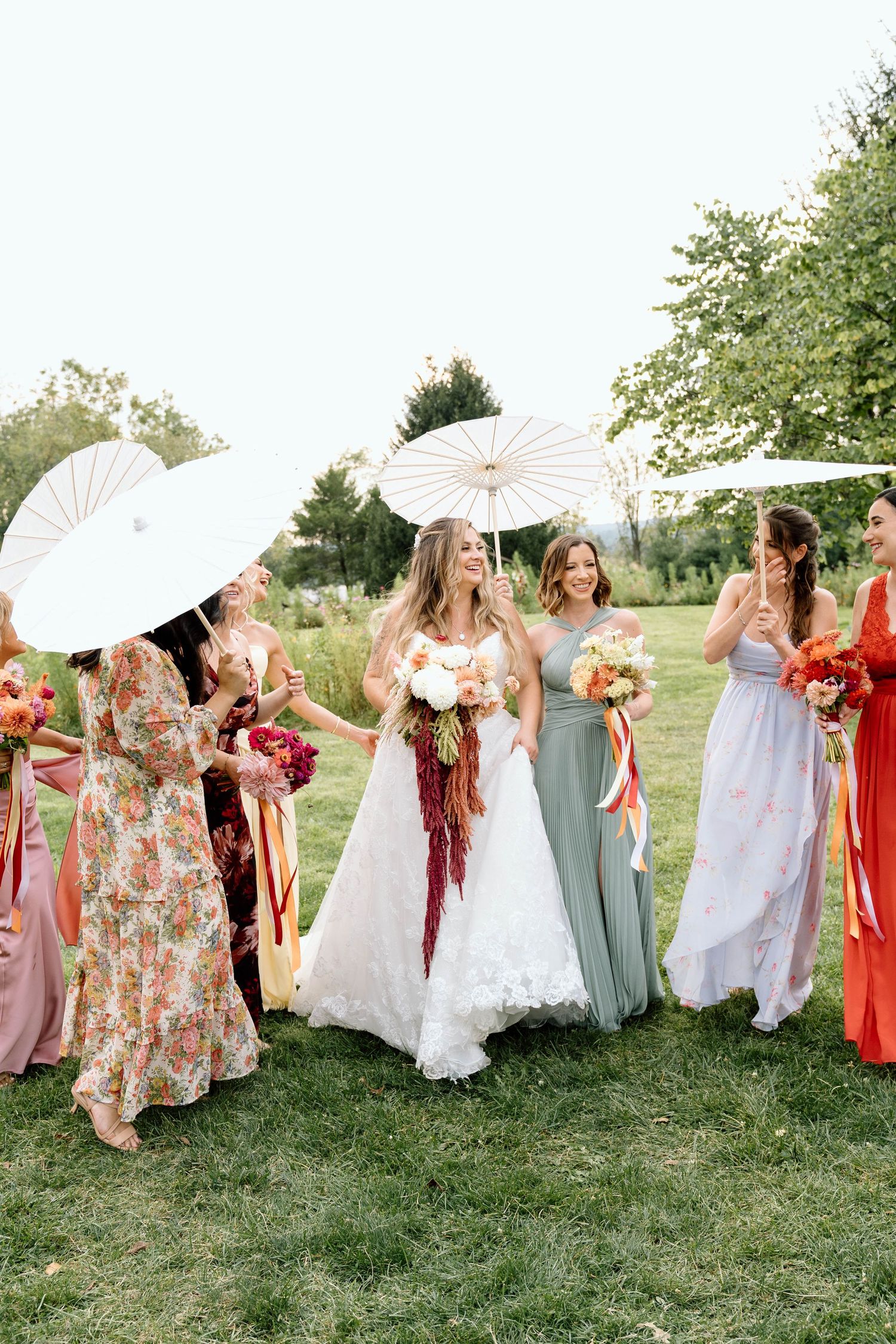 Bride laughing in a field with bridesmaids holding parasols