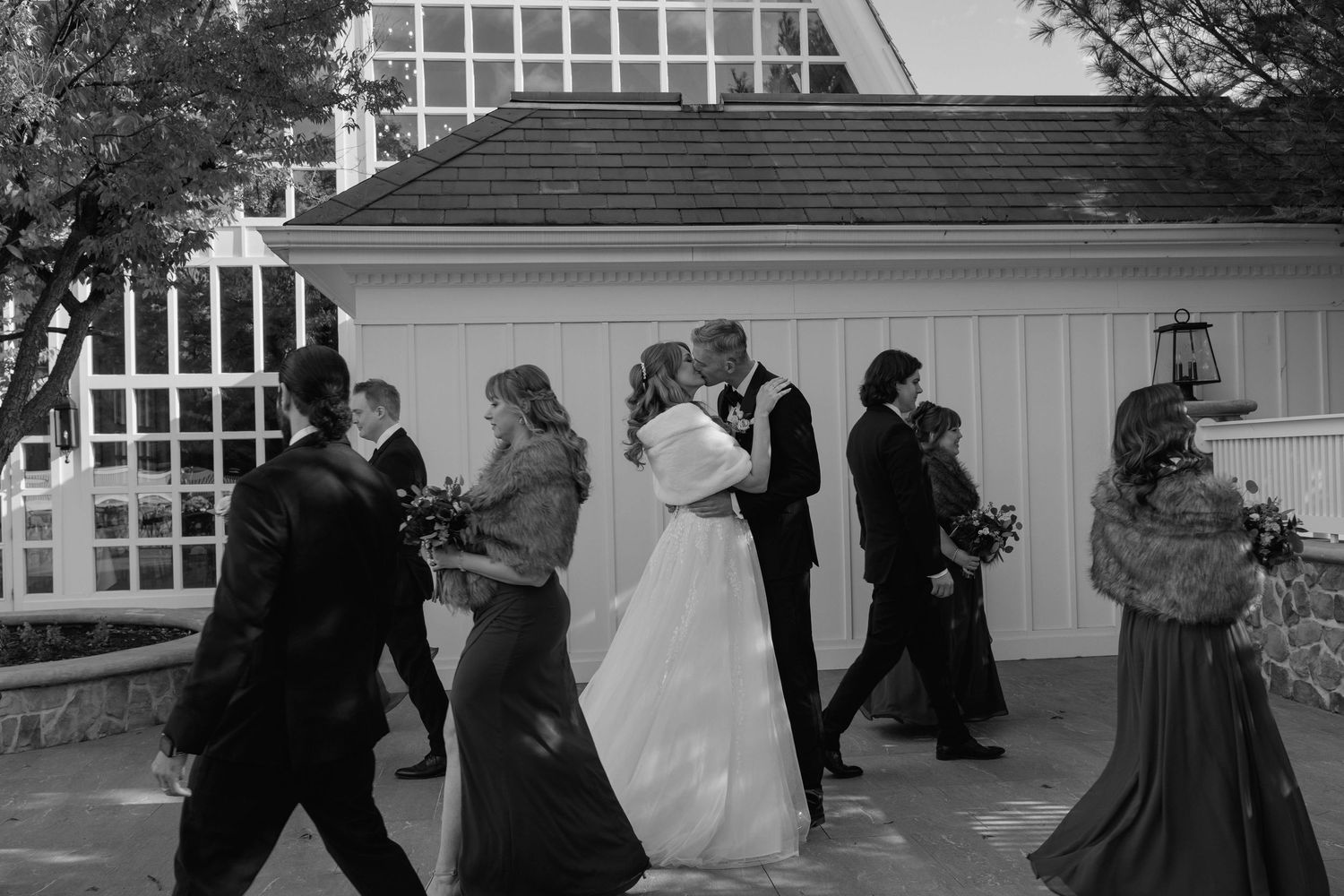 Bridal party walking past the bride and groom kissing