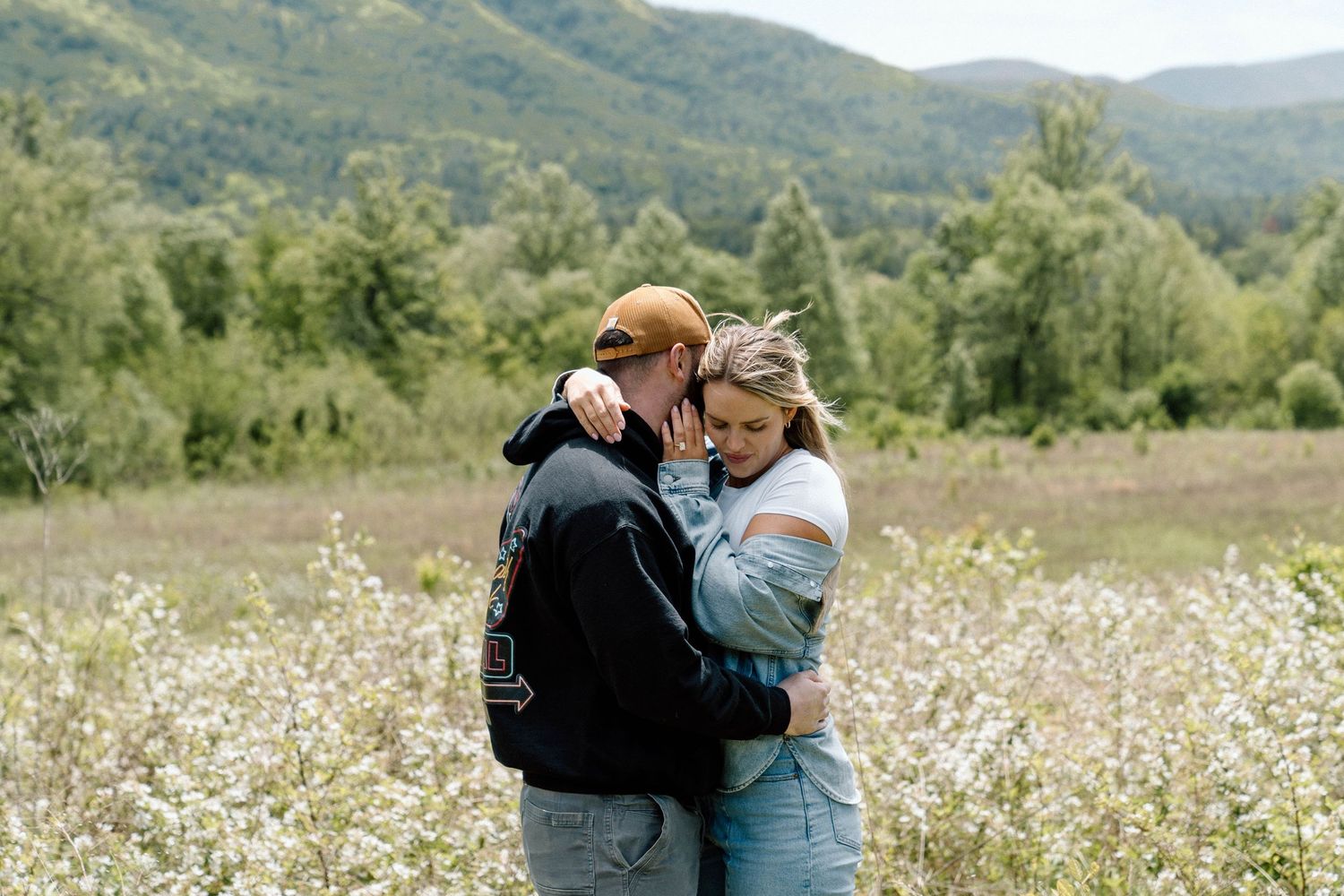 Man and woman hugging in a flower field with mountains behind them