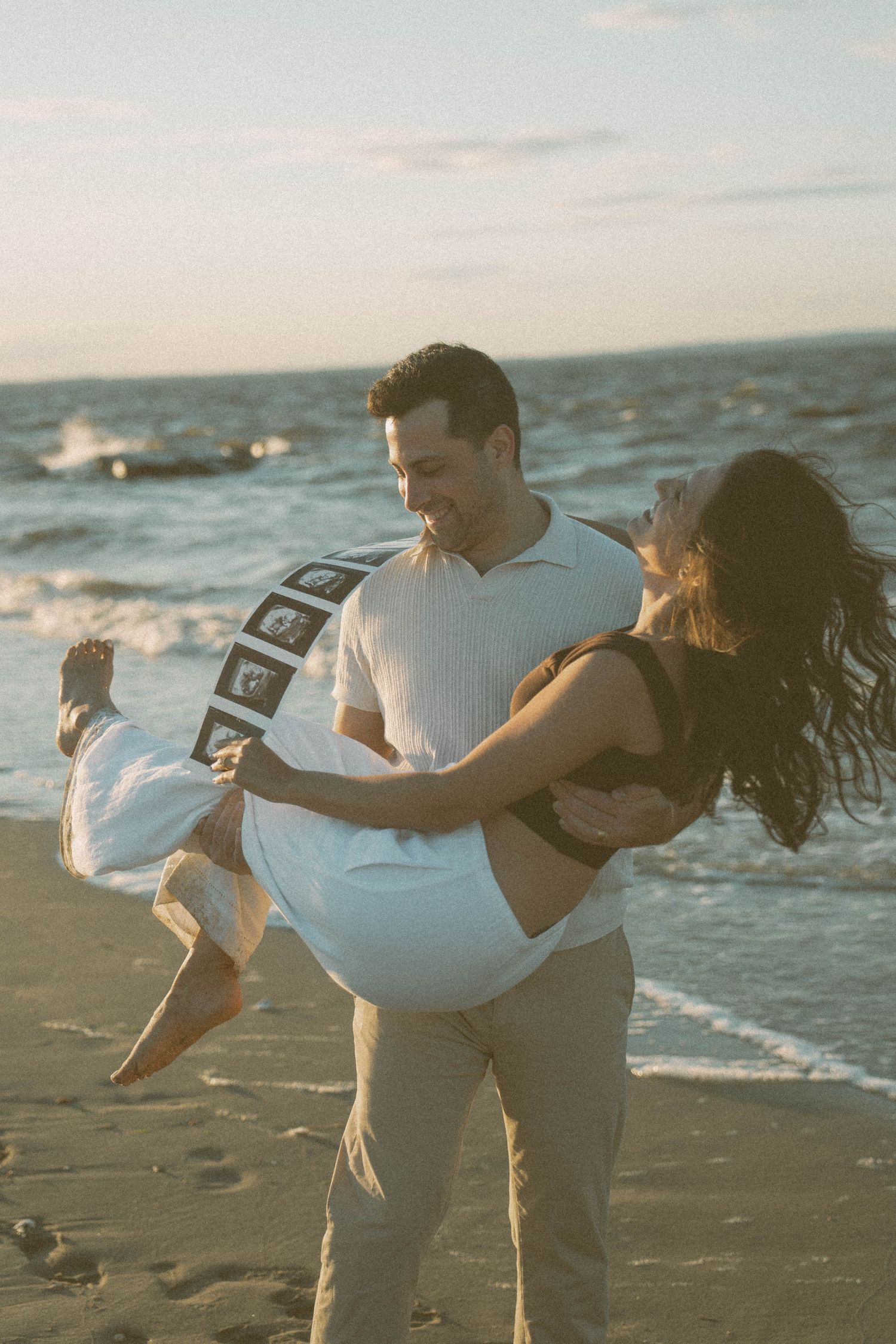 Man carrying a woman on the beach, holding ultrasound pictures