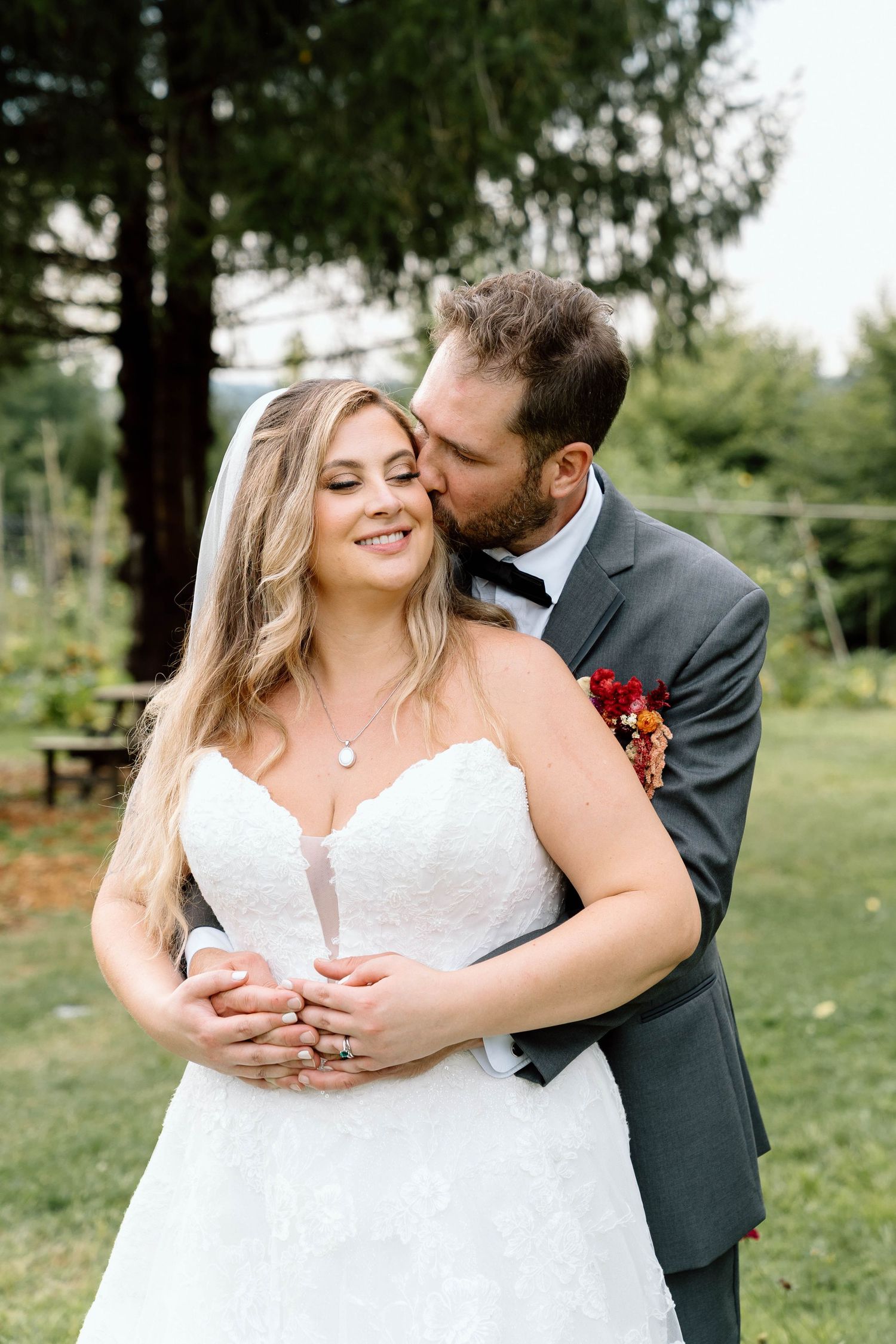 Groom embracing his bride around the waist and kissing her cheek