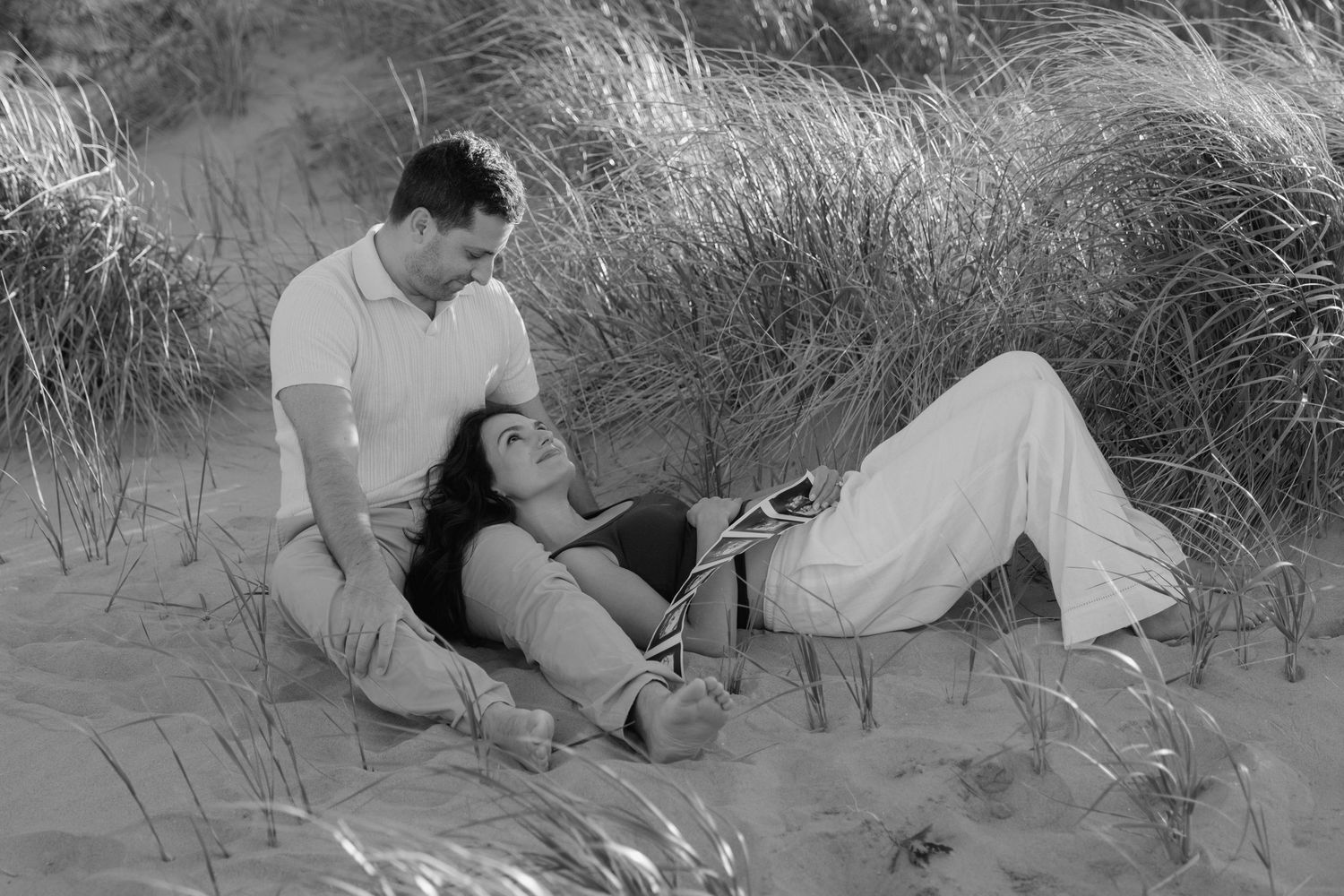 A woman lying on her husband's lap, holding ultrasound images next to her pregnant belly