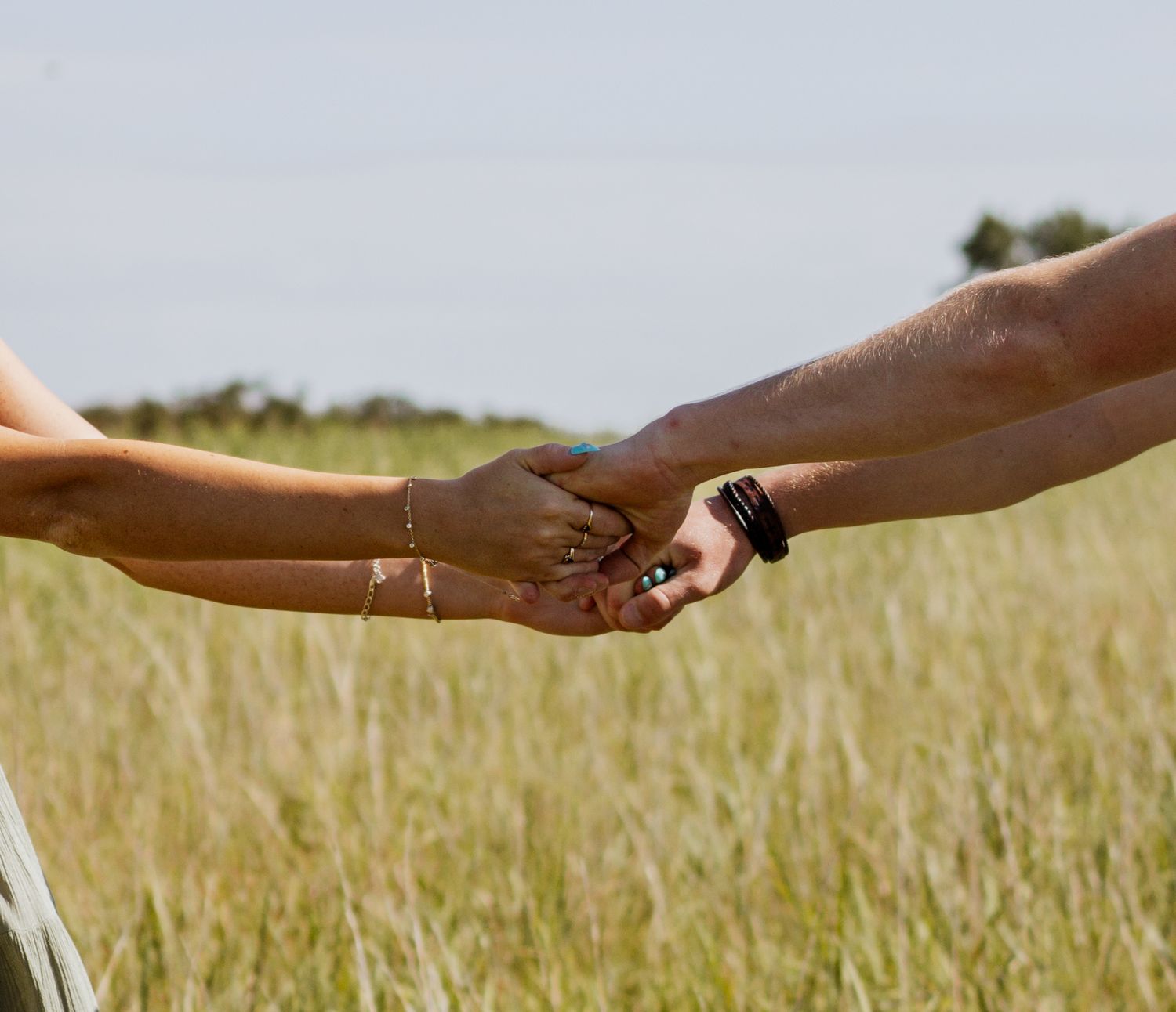 Two people holding hands in a field of tall golden grass, one wearing a bracelet and the other a smartwatch.