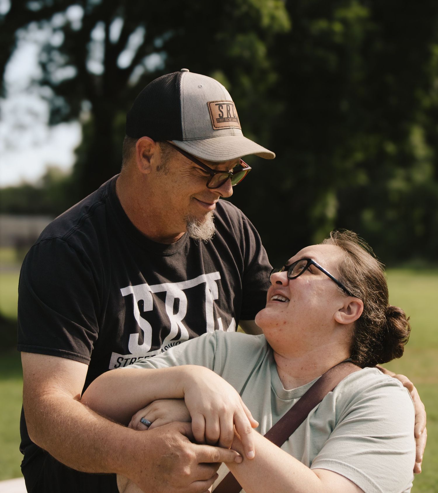 Couple laughing and holding hands joyfully outdoors in a sunny green park setting.