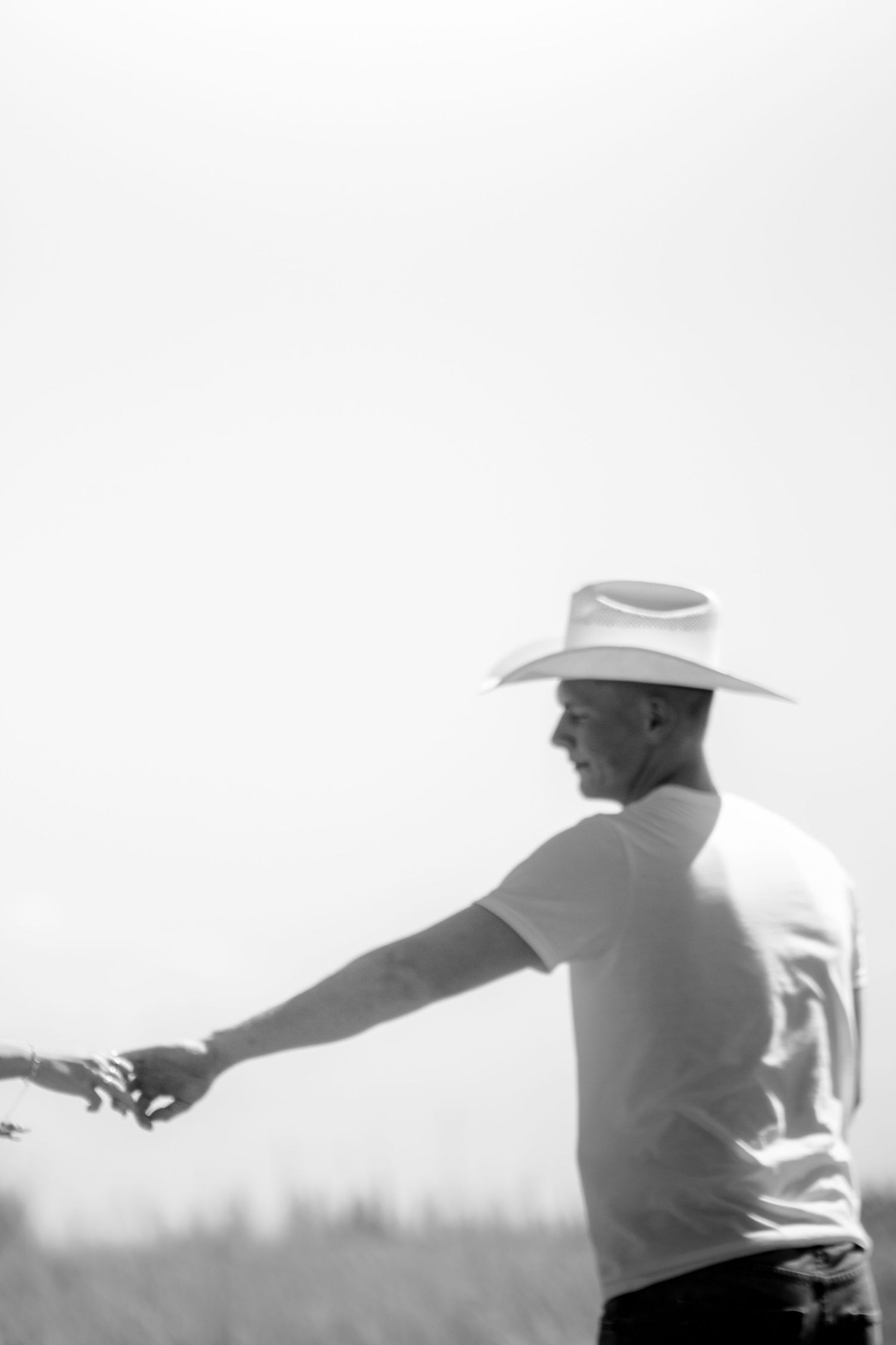 Black and white photo of a man in a cowboy hat reaching out his hand in a sunny field.