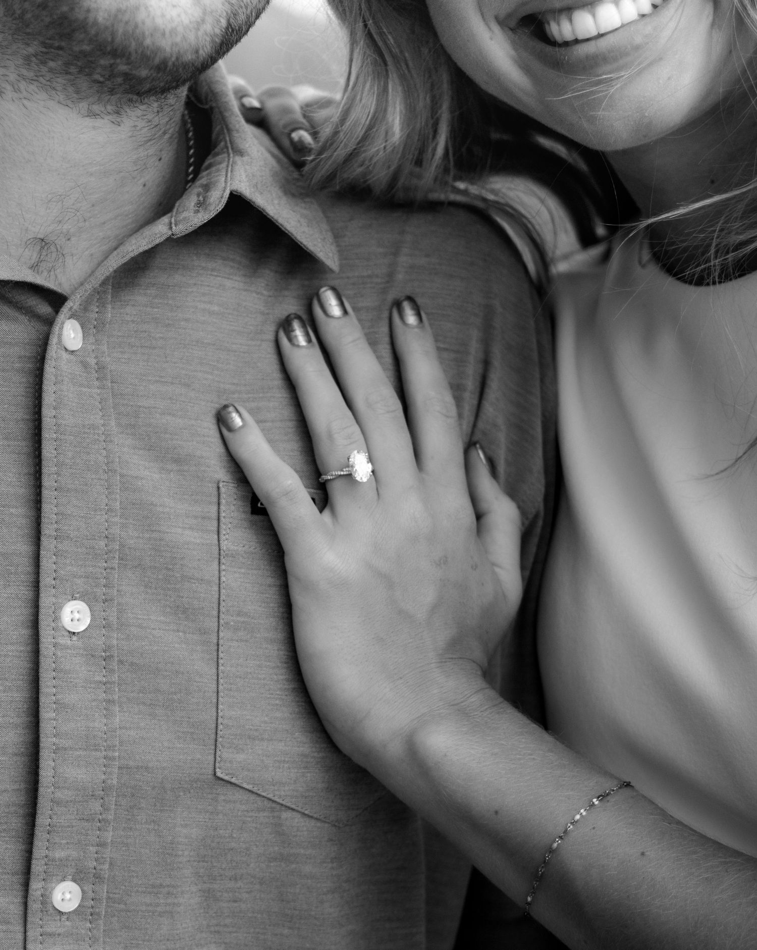 Close-up black and white photo of womans hand with engagement ring resting on mans gray shirt.