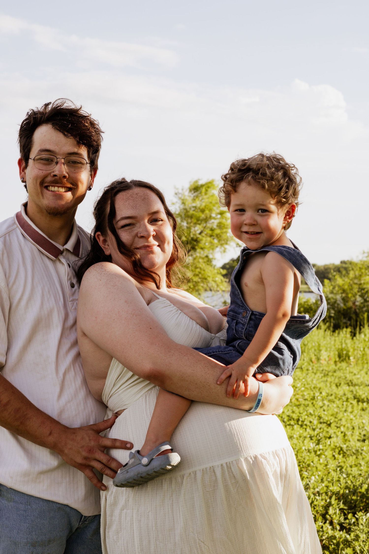 Happy young family with toddler posing outdoors in a green field on a sunny day.