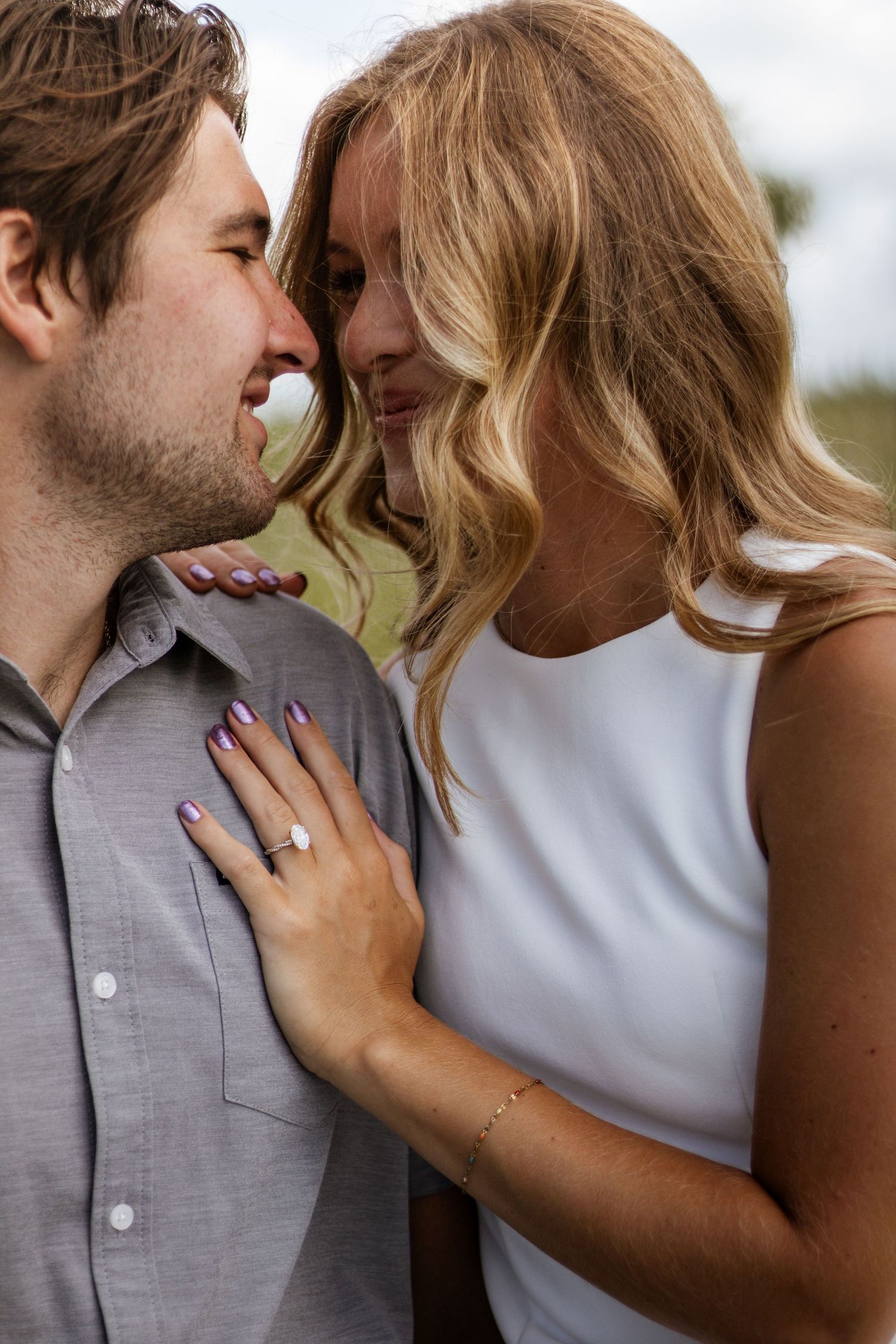 Couple sharing a romantic moment, woman in white dress with engagement ring resting hand on mans chest.