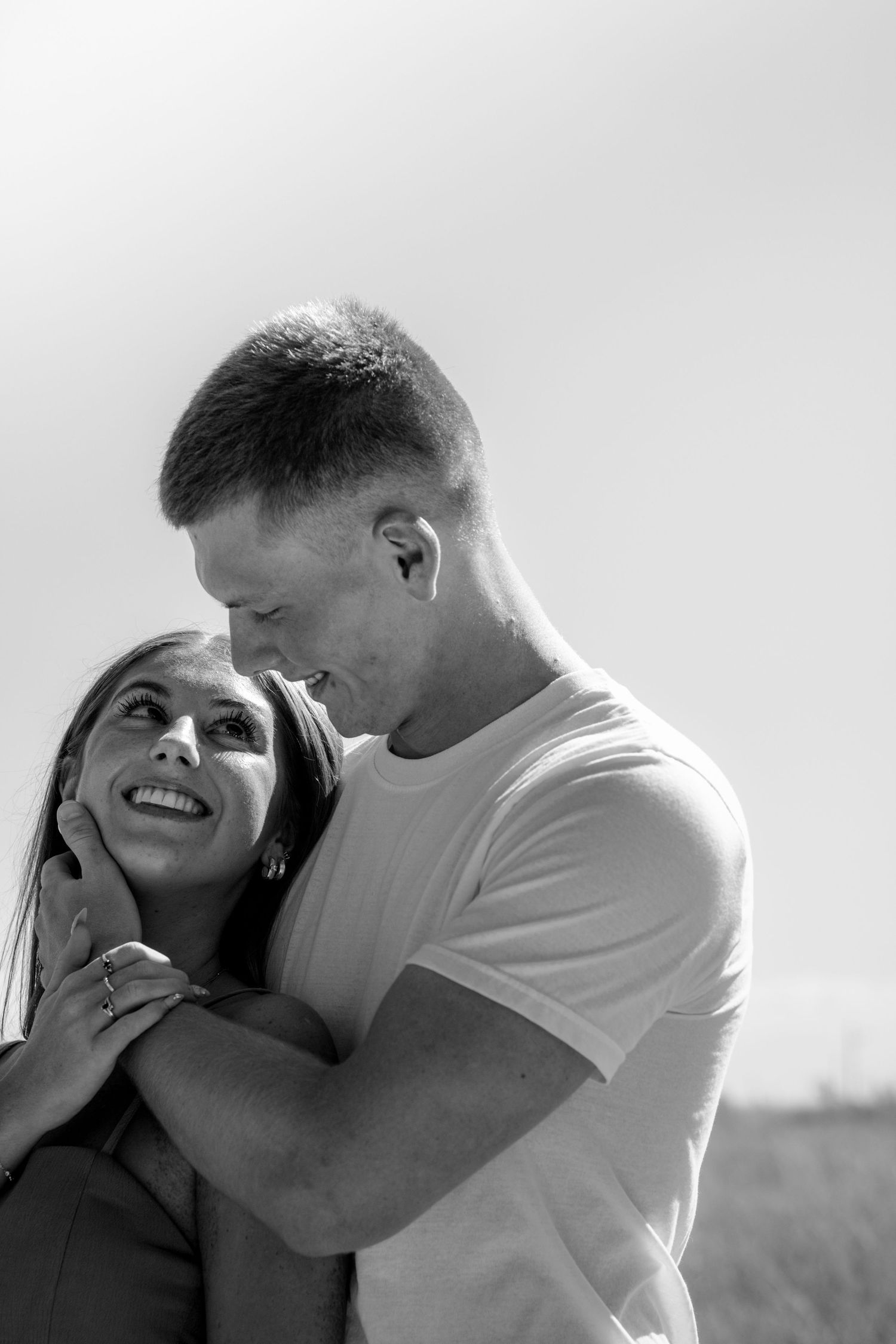 Black and white photo of a loving couple embracing outdoors, woman smiling up at man in a tender romantic moment.