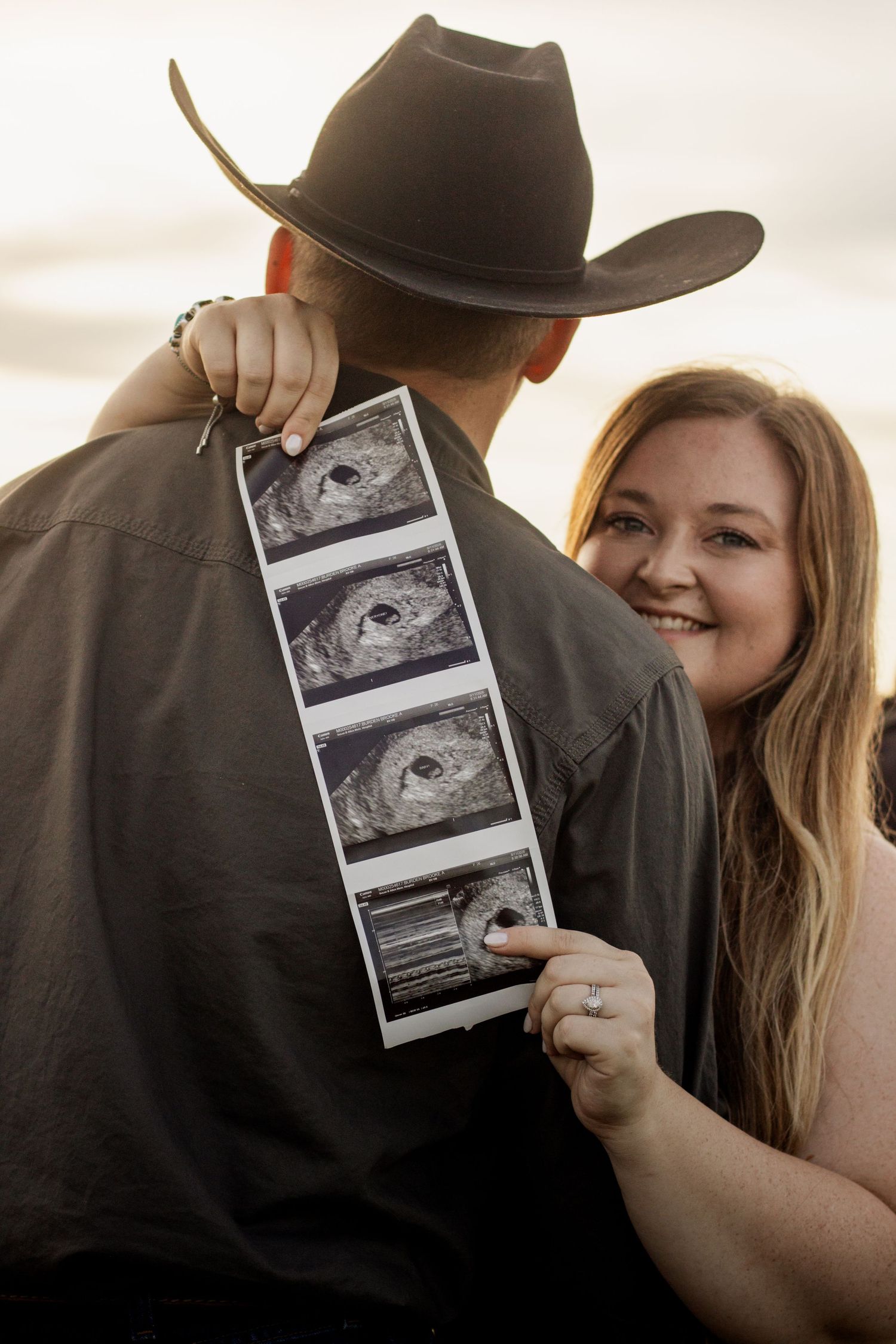 Happy couple embracing outdoors holding ultrasound photos, pregnancy announcement at golden hour sunset.