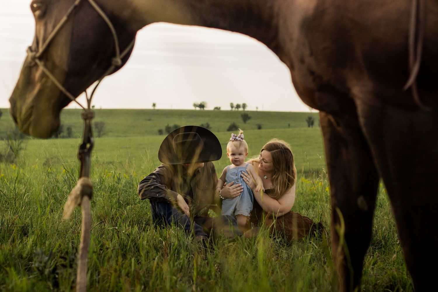 Family with baby enjoying a sunny day in green field with brown horse in foreground on a farm.