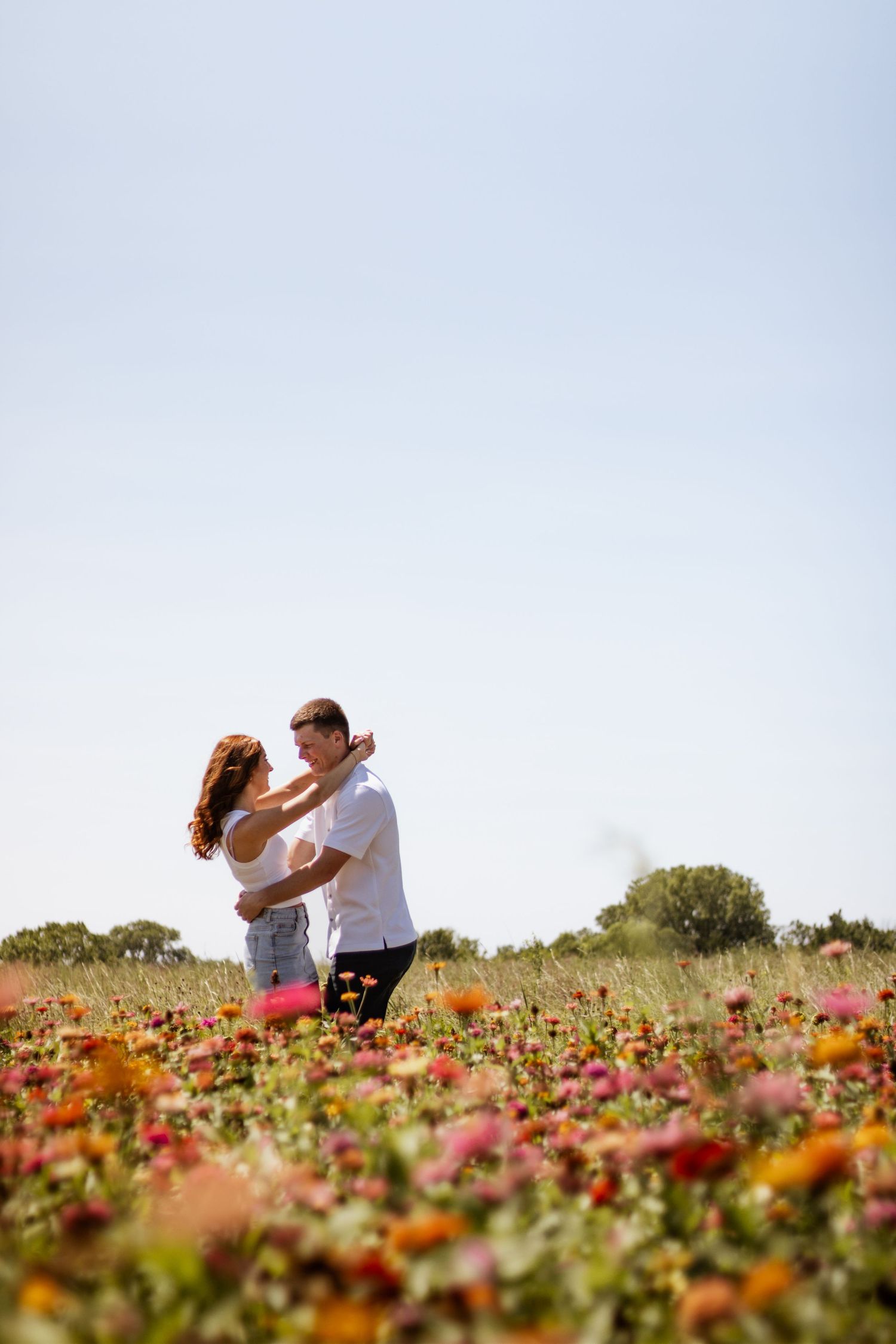 Romantic couple dancing together in a vibrant colorful flower field under a clear blue sky.