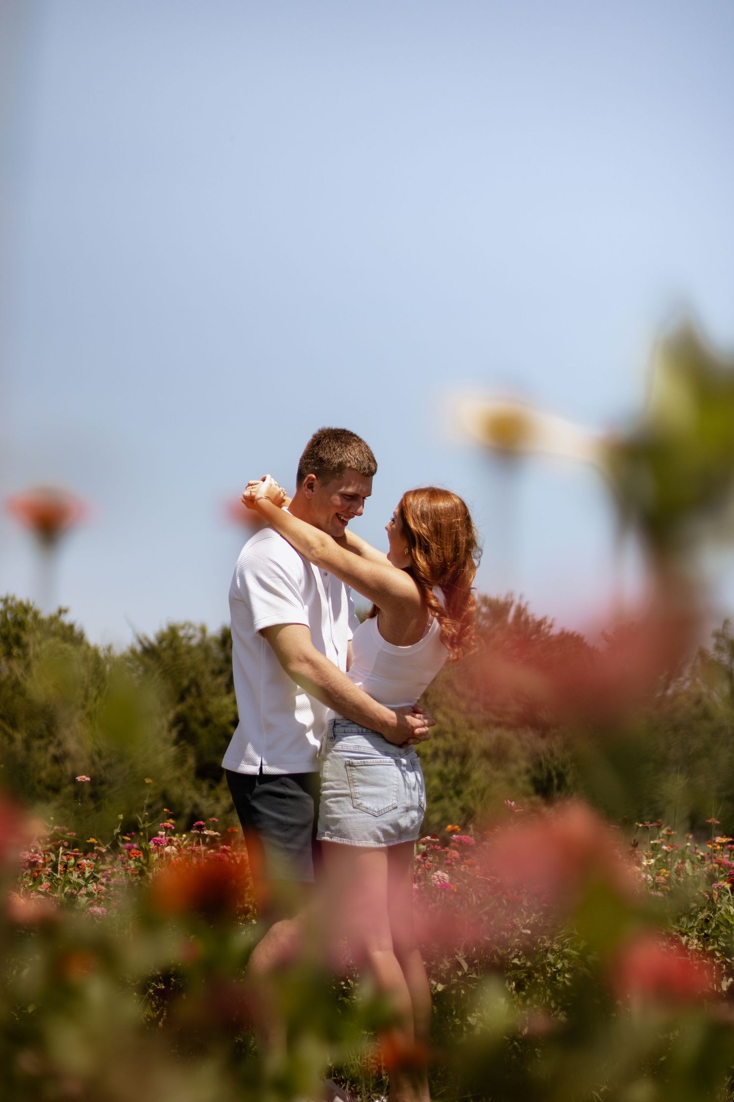 A romantic couple embraces in a colorful flower garden under a clear blue sky on a sunny day.