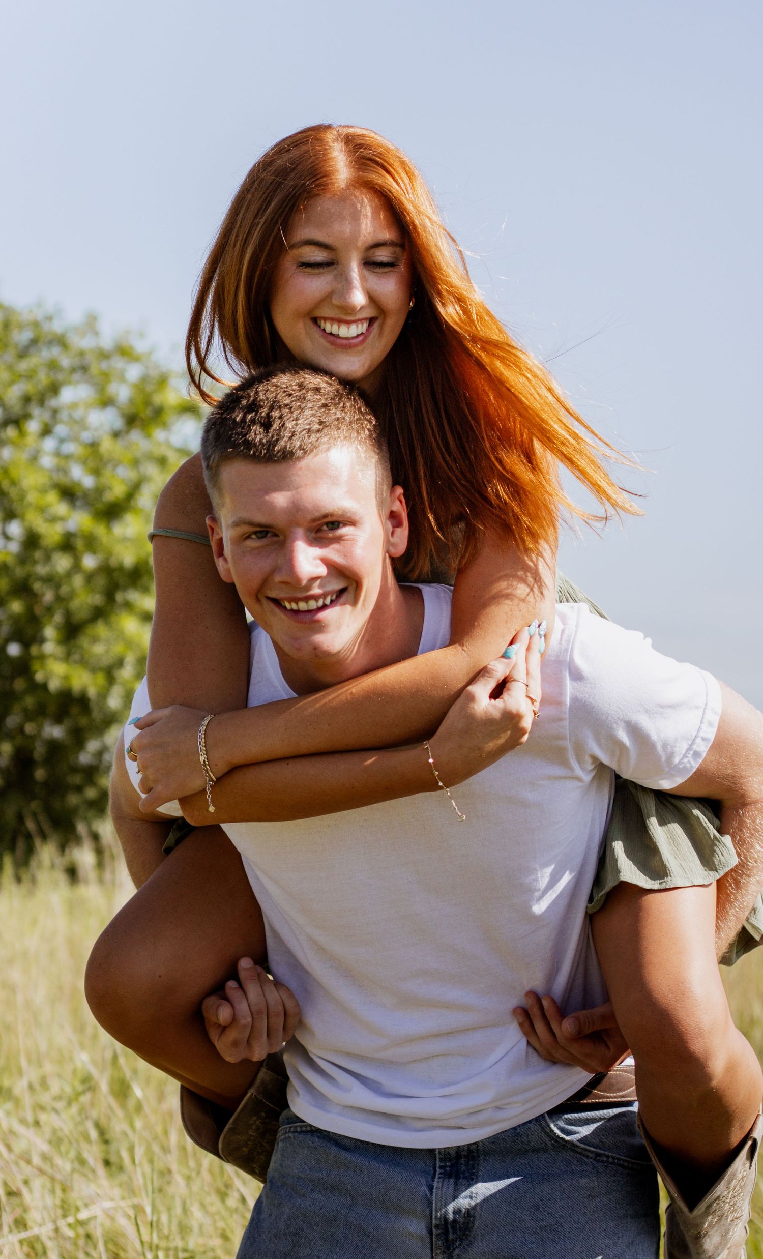 A happy young couple enjoying a sunny day outdoors, with a woman riding piggyback on a smiling man in a field.