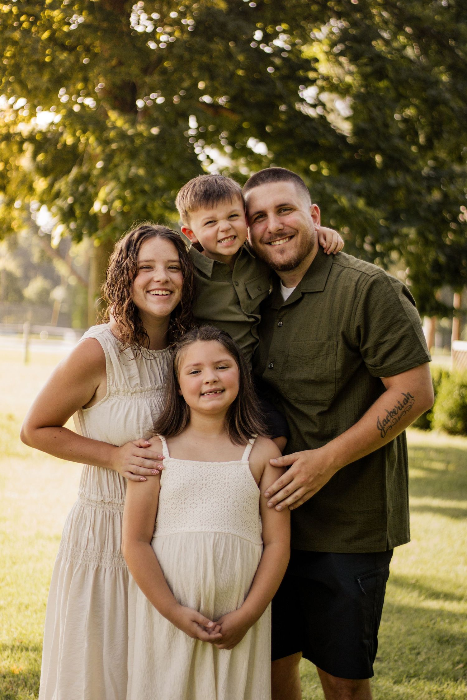 Happy family of four posing outdoors at golden hour, parents with son and daughter in a park.