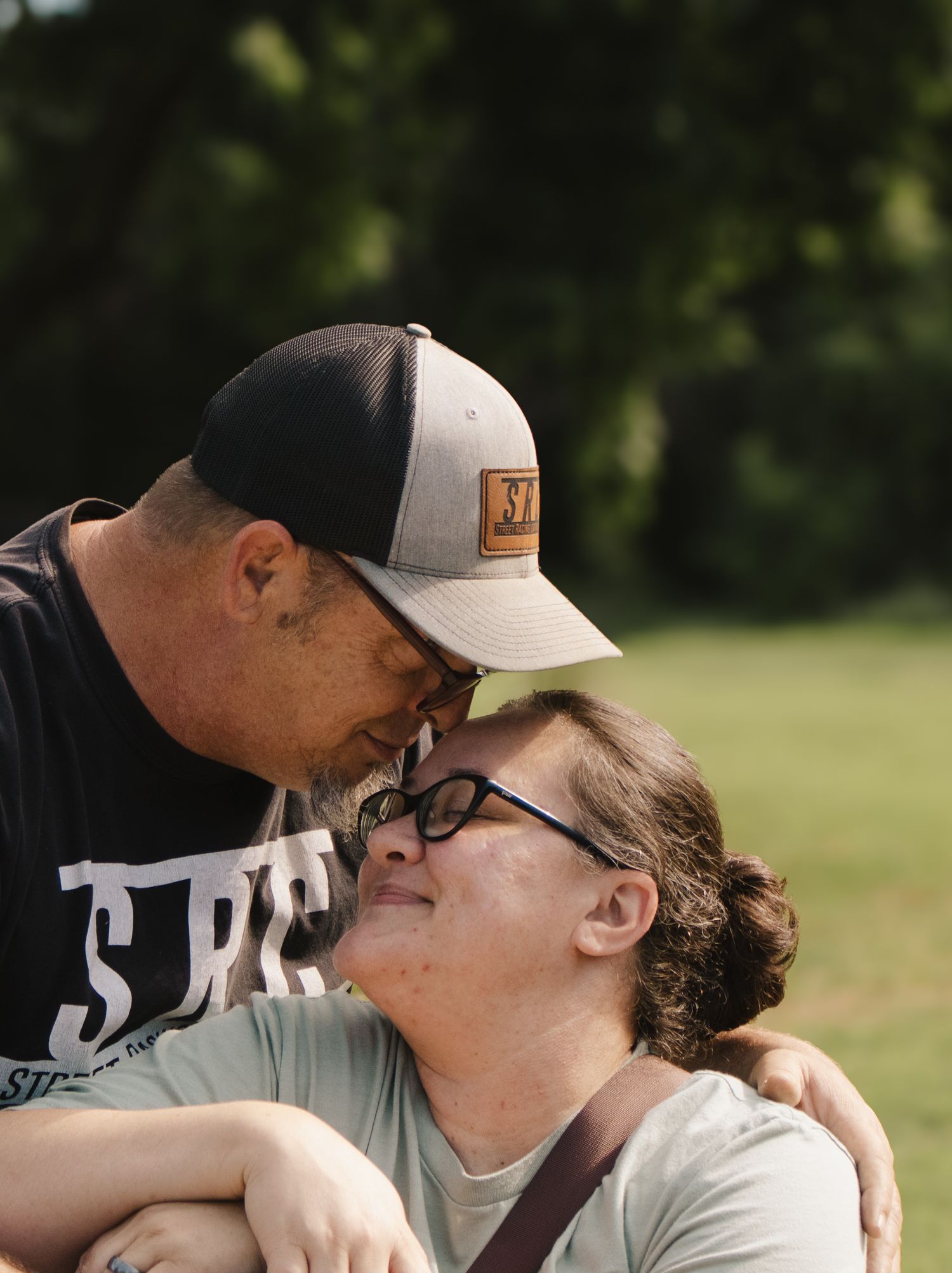 Man leaning in to kiss woman on the cheek outdoors, sharing a tender romantic moment in a park.