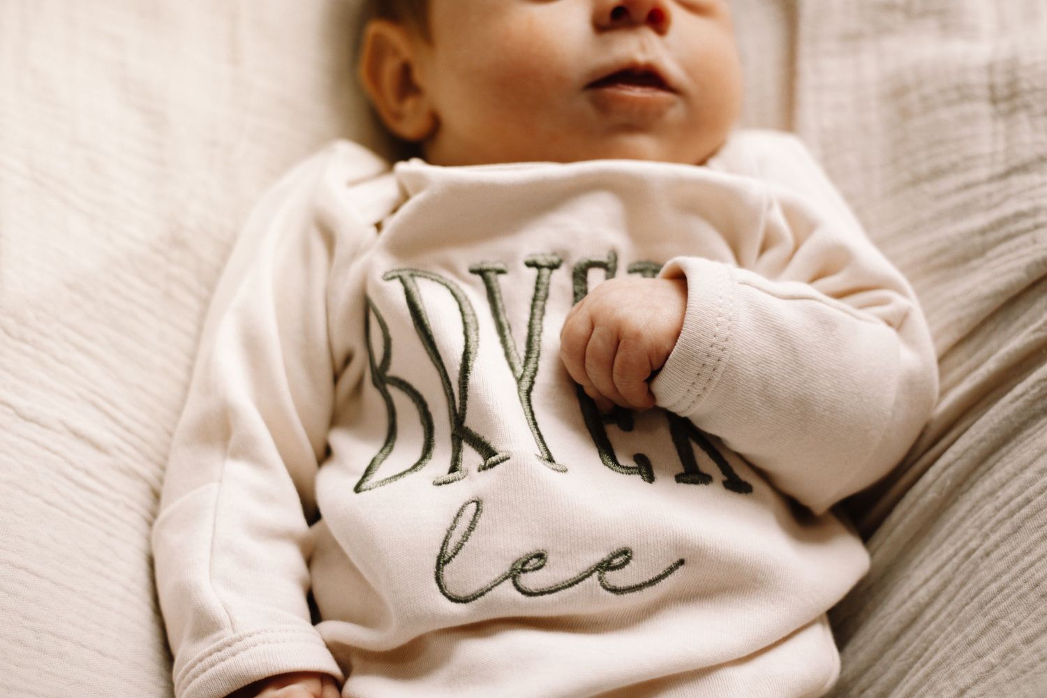 Newborn baby wearing personalized embroidered name romper lying on soft blanket.
