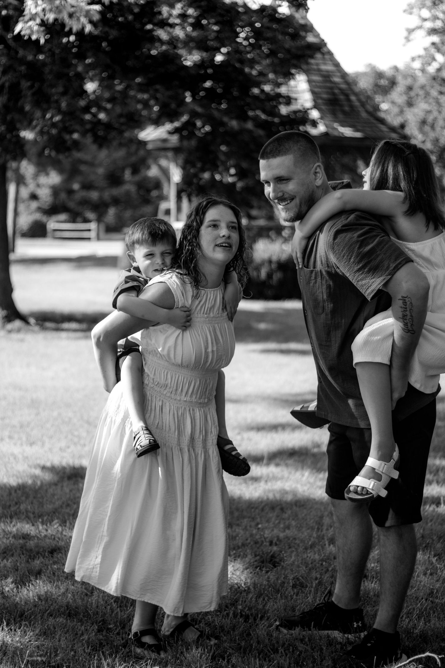Black and white photo of a smiling family with children outdoors in a park setting on a sunny day.