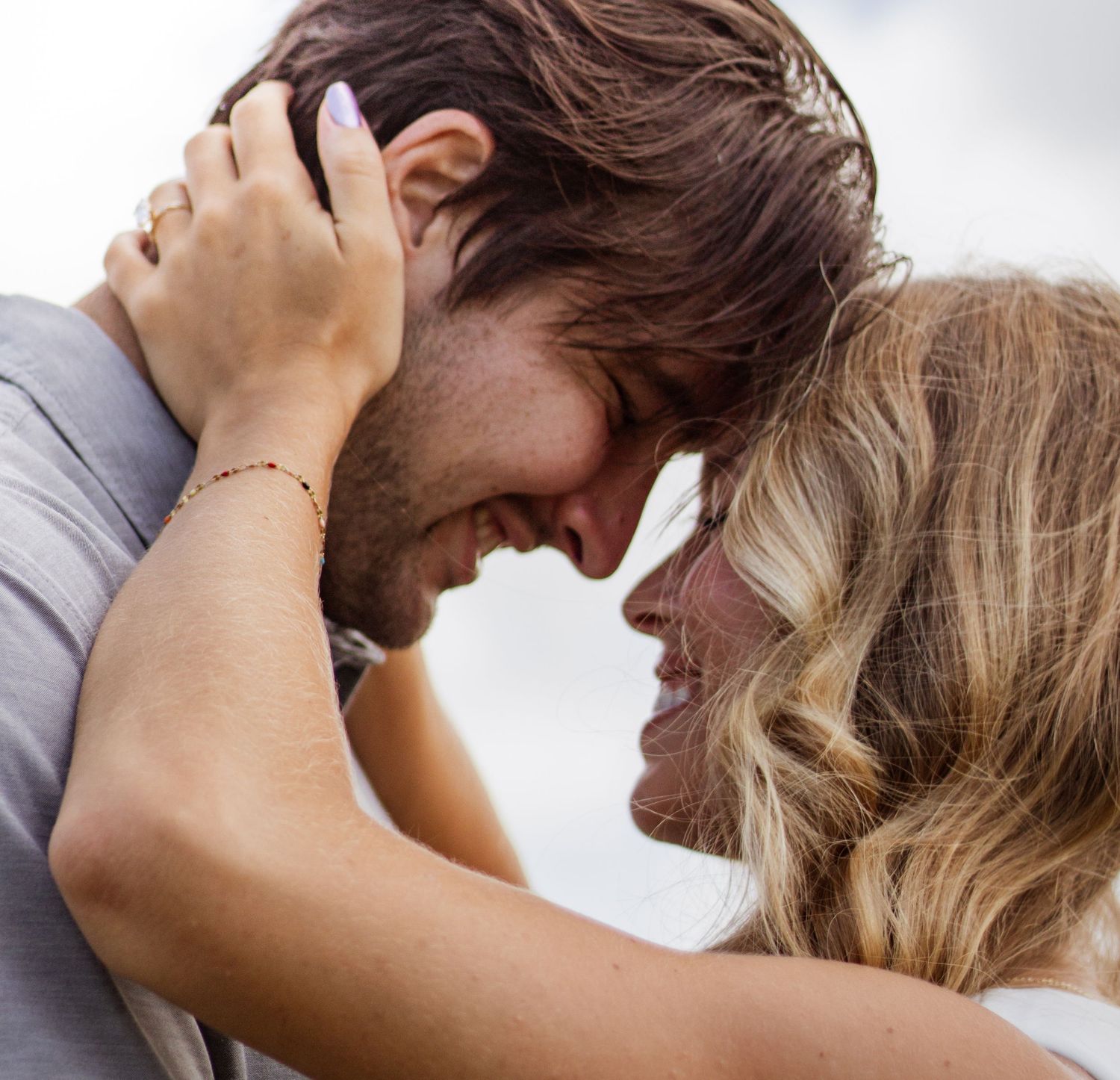A smiling couple sharing a romantic forehead-to-forehead moment, embracing tenderly outdoors on a cloudy day.