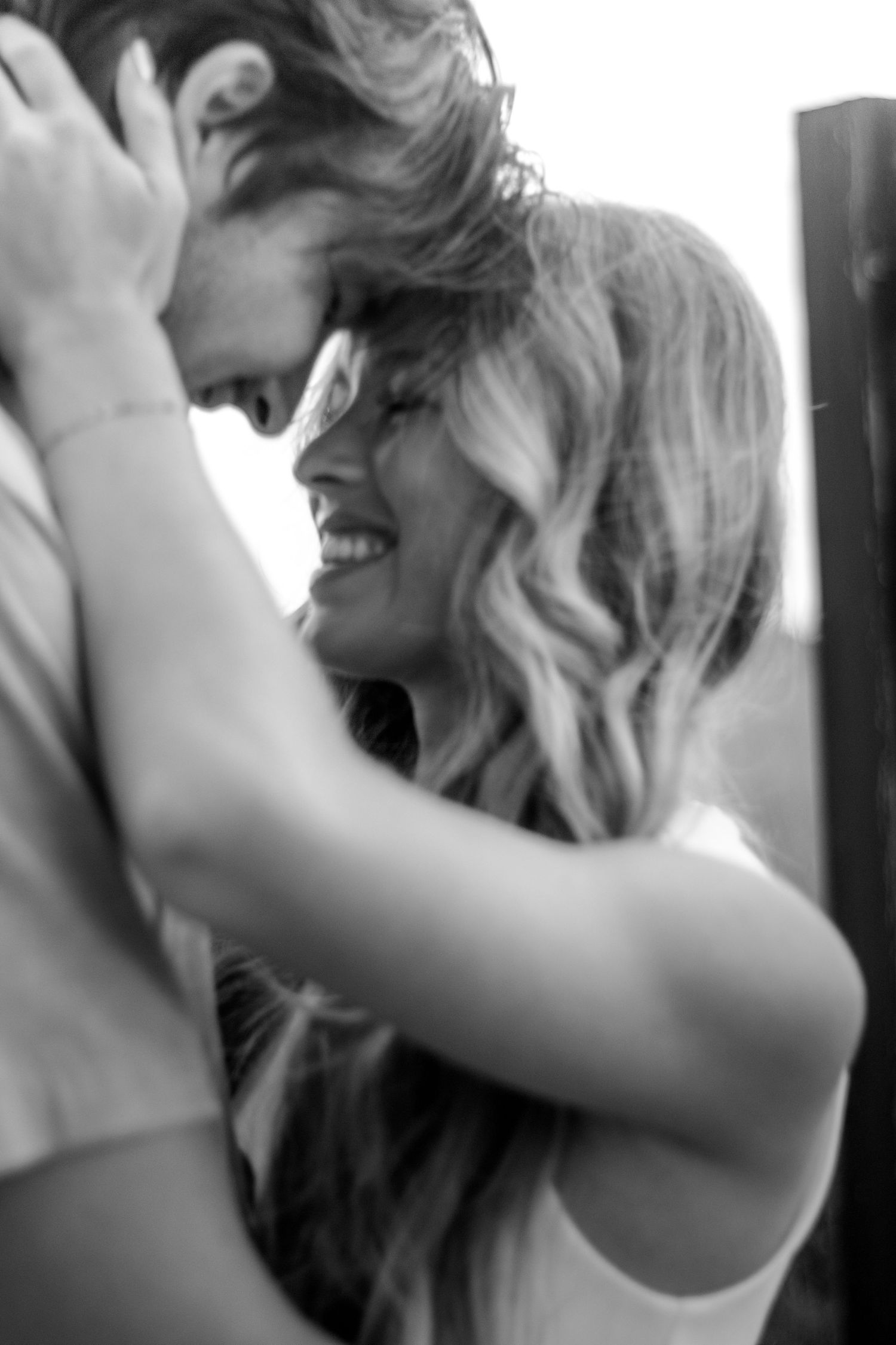 Couple sharing an intimate moment, foreheads touching and smiling in a black and white photo.