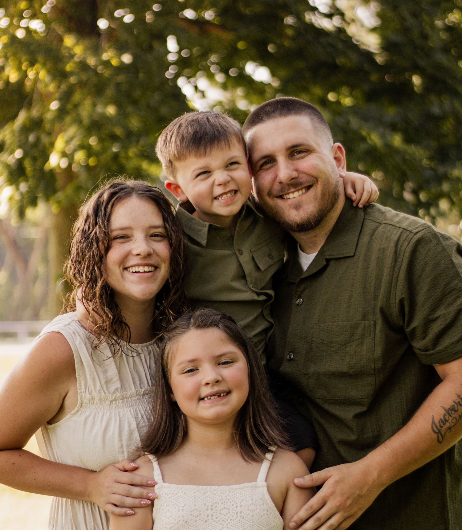 Smiling family of four posing outdoors, father in green shirt with two daughters and young son.