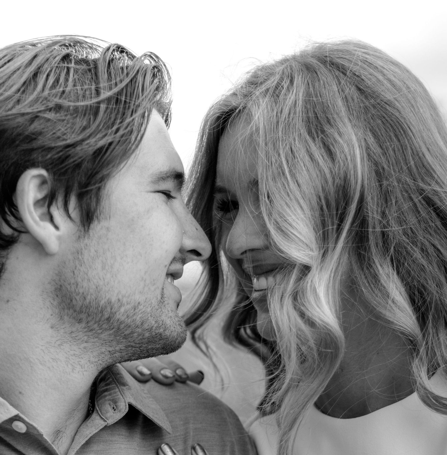 A joyful couple gazes at each other closely in this intimate black and white portrait outdoors.