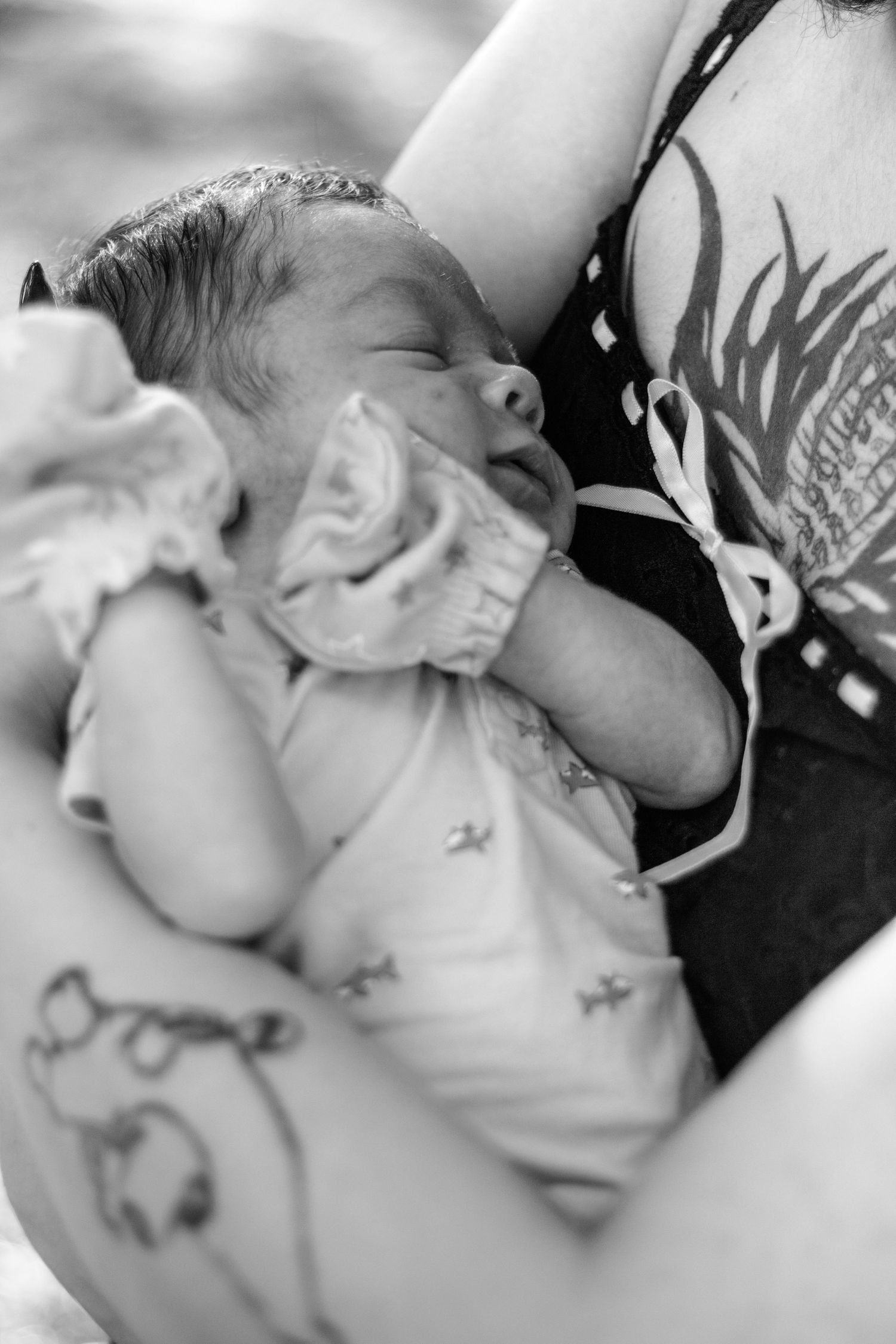Black and white photo of a sleeping newborn baby cradled in the arms of a tattooed mother.