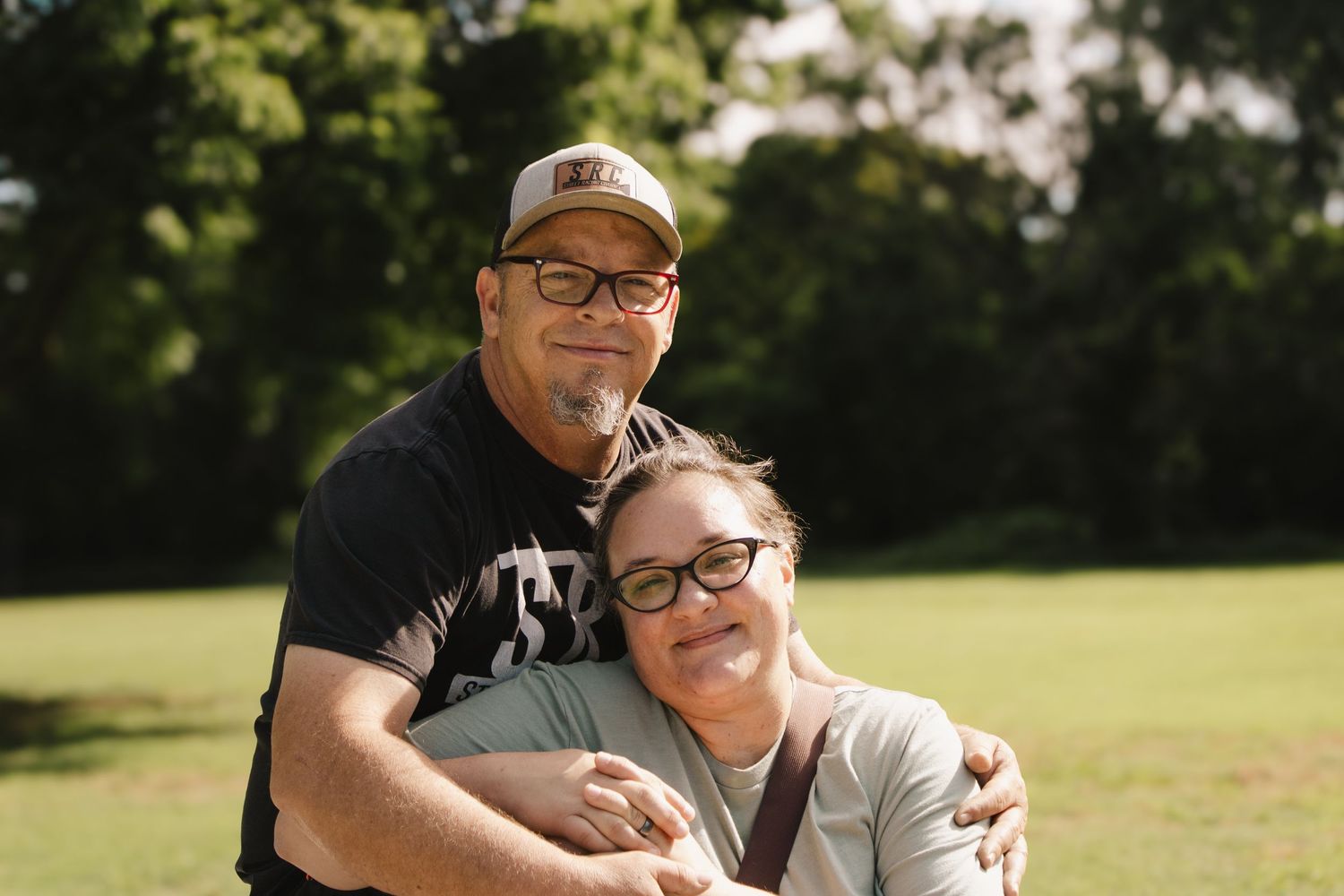 Loving couple embraces and smiles together outdoors in a sunny green park setting.