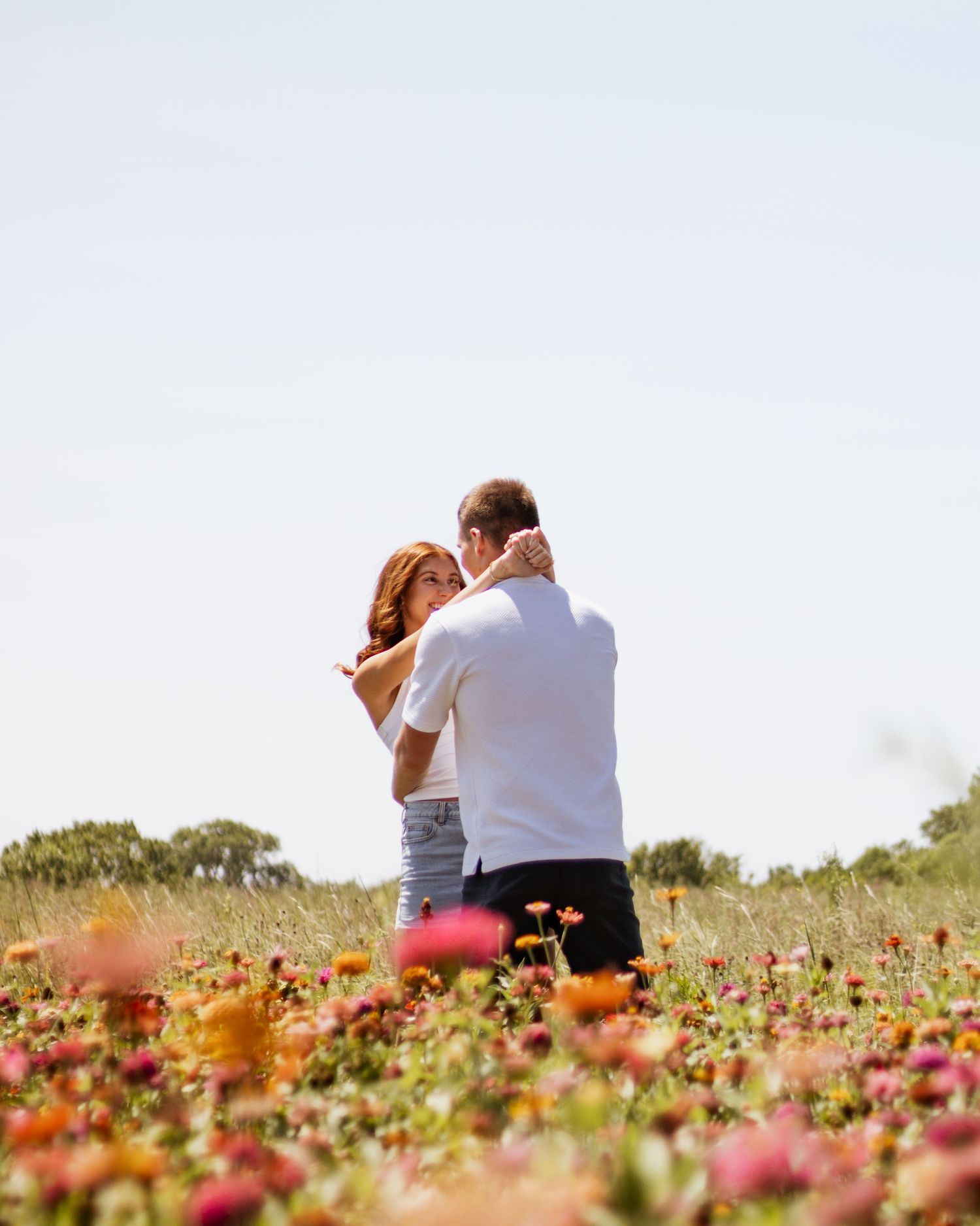 Couple embracing in a vibrant colorful flower field under a bright clear sky.