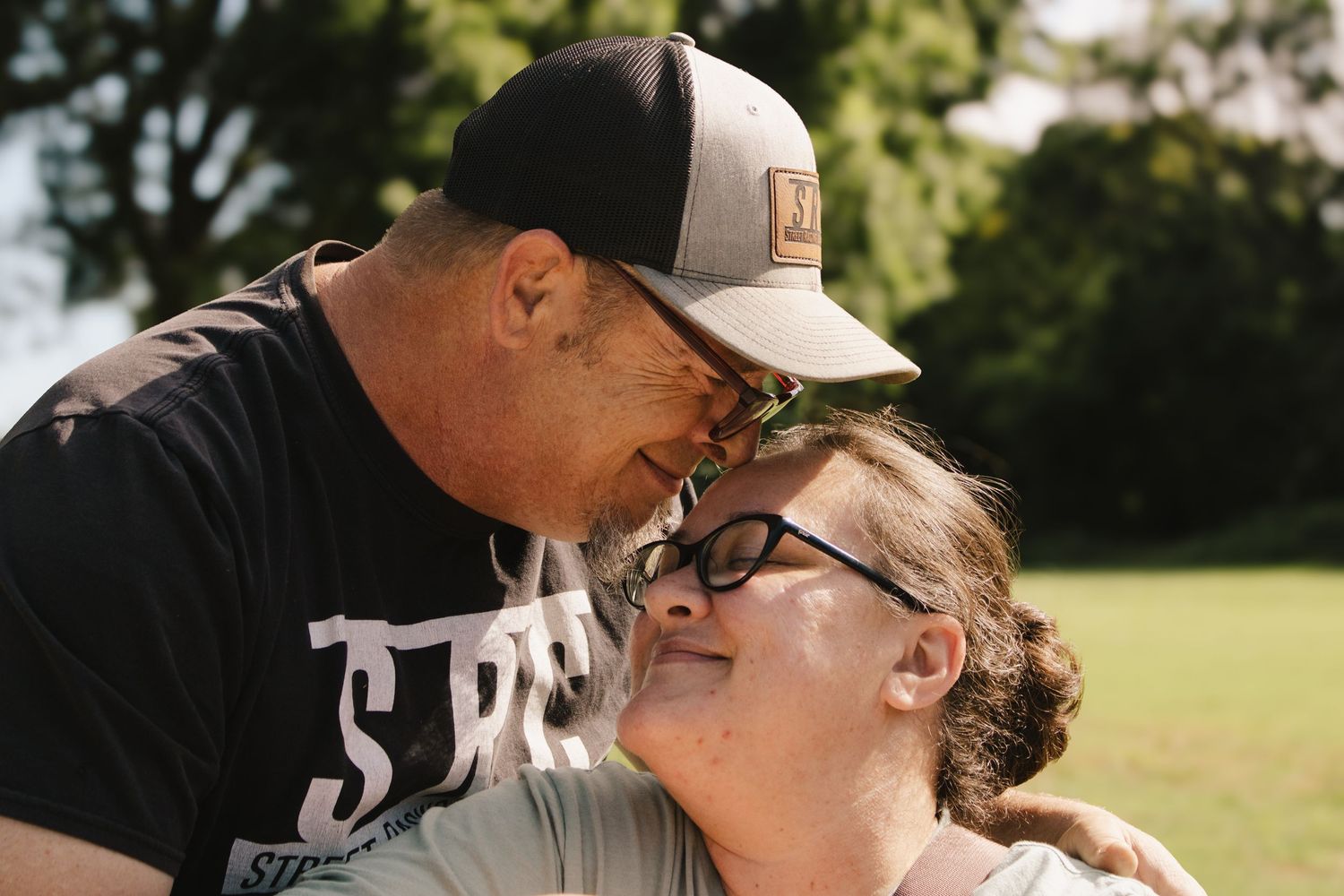 Couple laughing and sharing an intimate close moment together outdoors in sunny park.