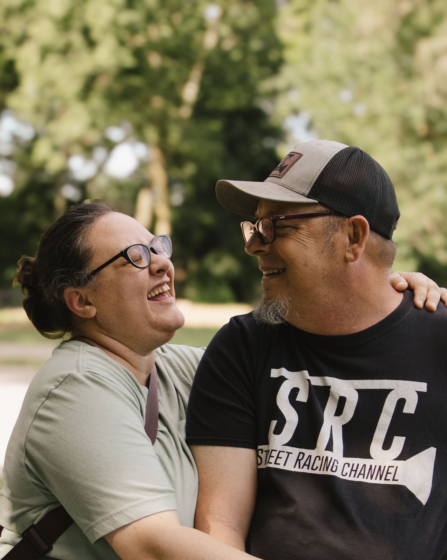 Couple laughing and gazing at each other outdoors in a sunny park, sharing a joyful moment together.
