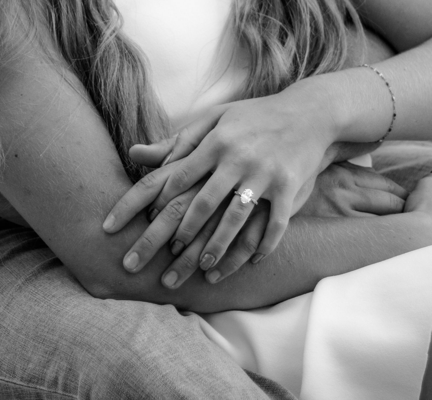 Close-up black and white photo of couple embracing, woman displaying diamond engagement ring on her finger.